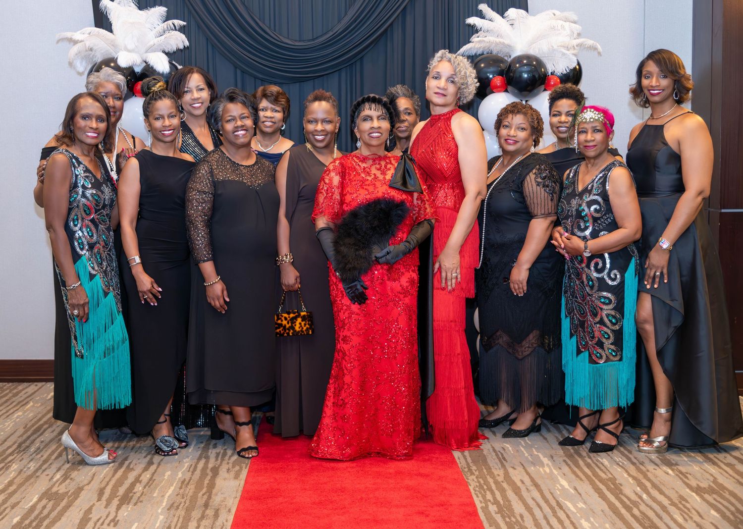 Group of elegantly dressed women posing together at a formal gala event on a red carpet.
