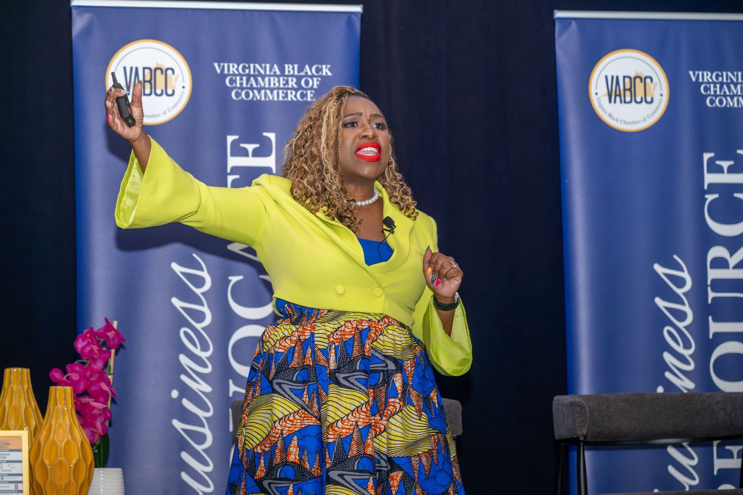 Woman in yellow blazer and African print skirt speaks energetically at Virginia Black Chamber of Commerce event.
