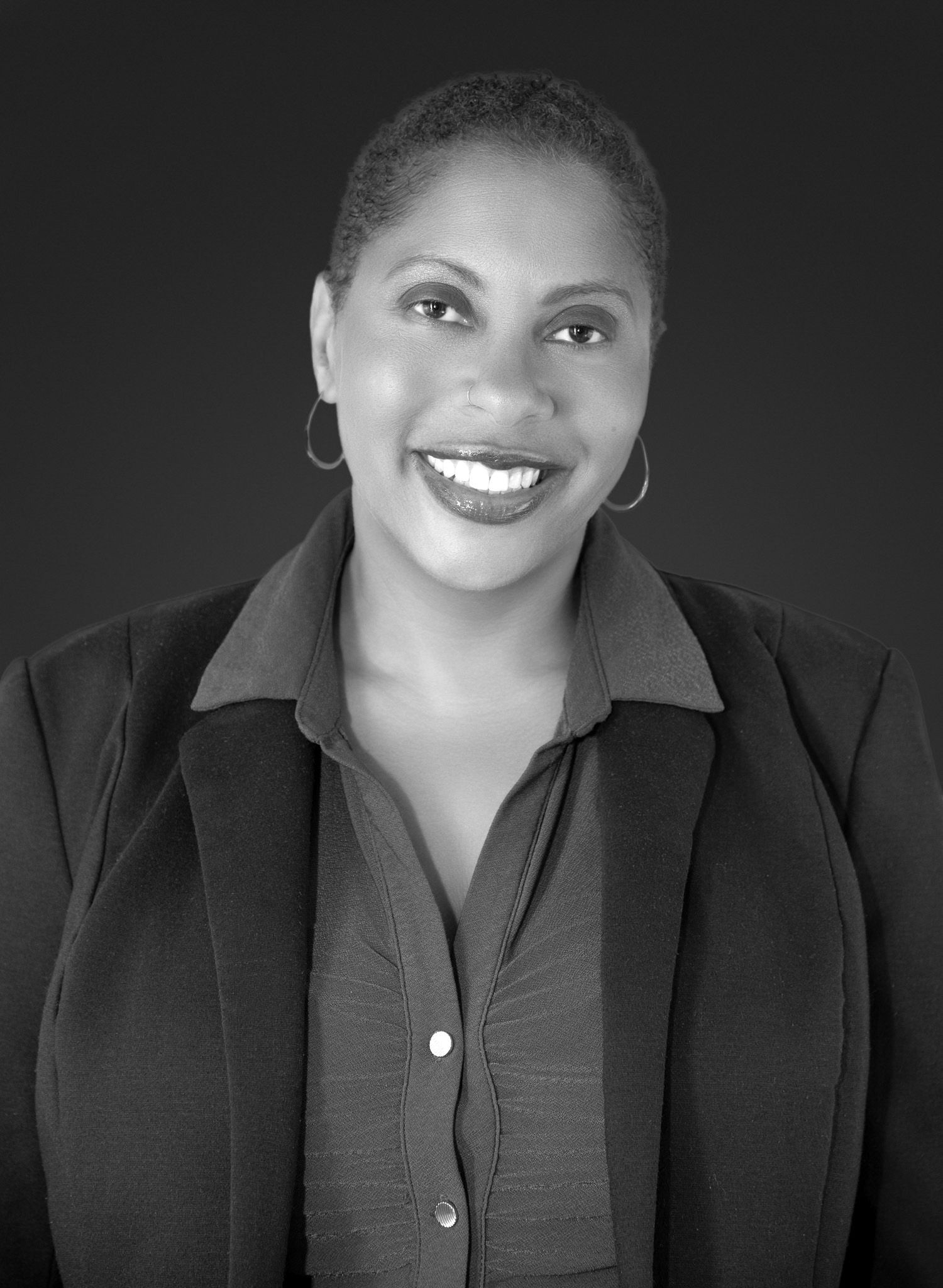 Professional black and white headshot of a smiling woman wearing hoop earrings and a blazer.