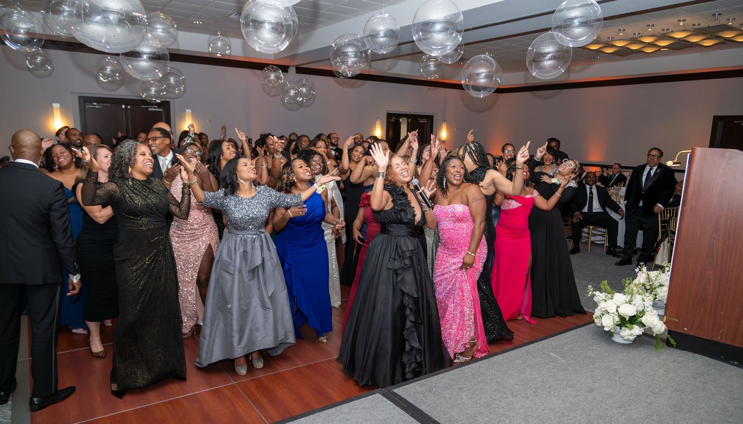 Elegant gala event with guests in formal attire reaching for bubbles in a decorated ballroom.