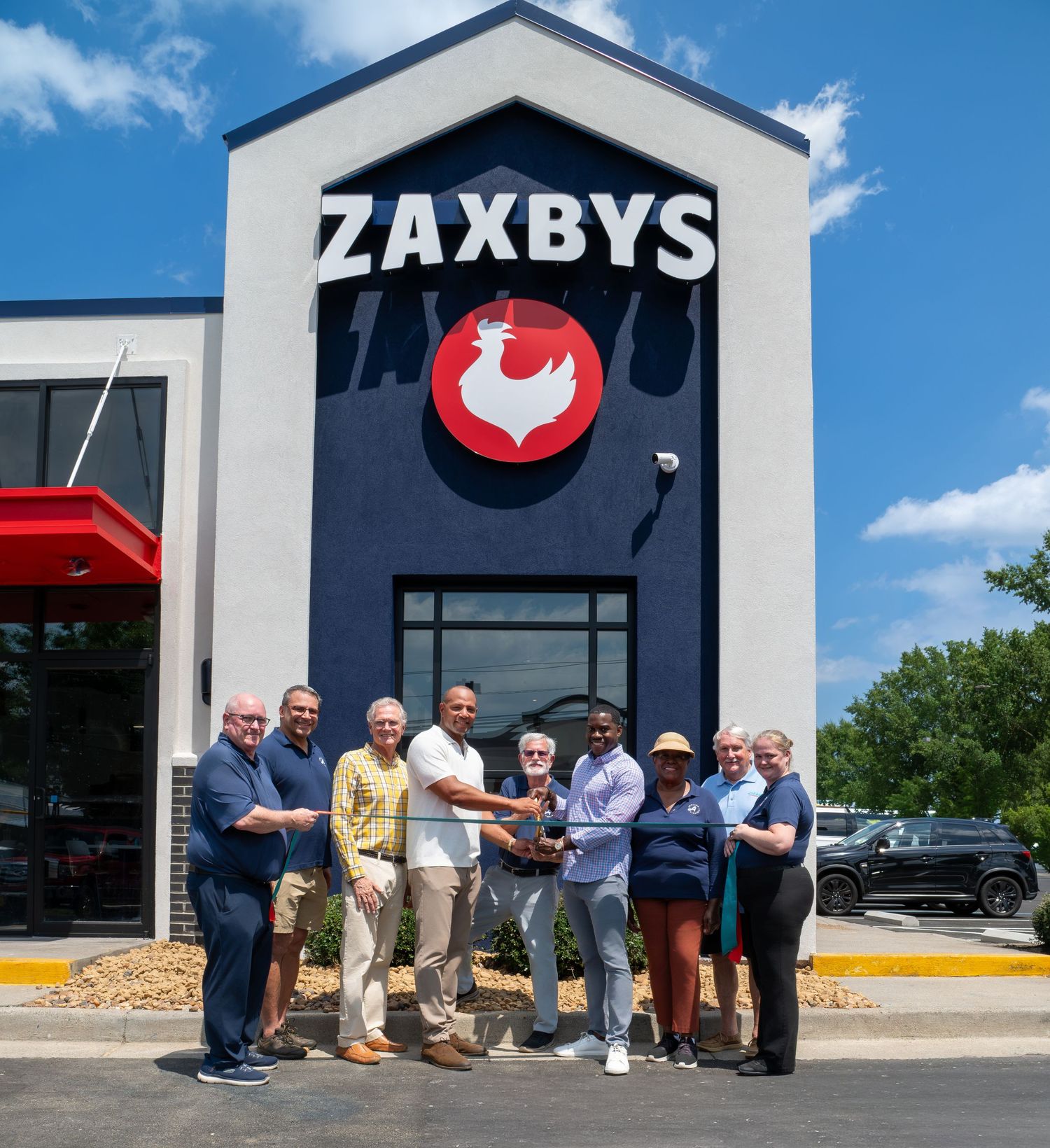 Group of people posing together in front of a Zaxbys restaurant on a sunny day.