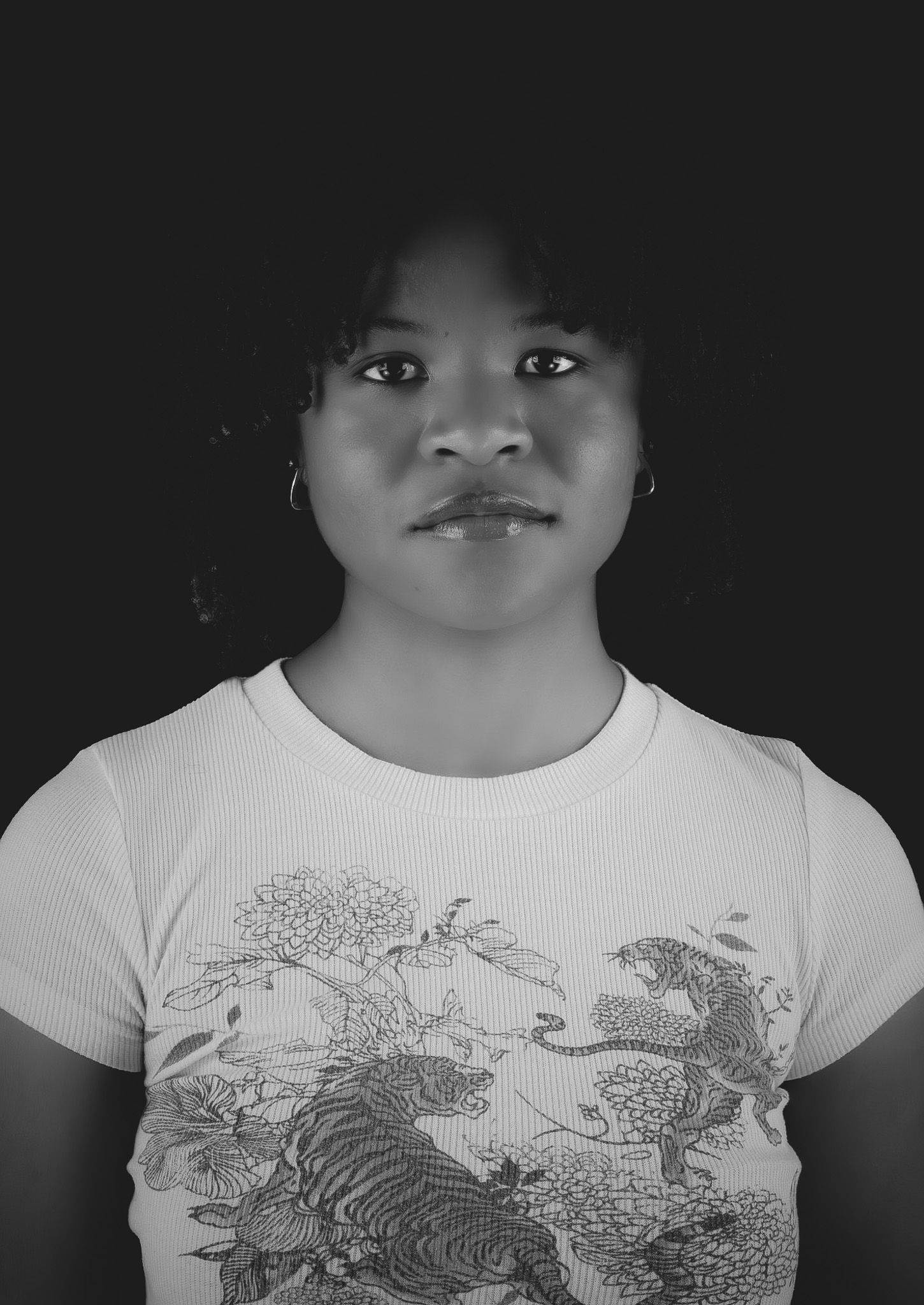 Black and white portrait of a young woman in a floral tiger graphic tee against a dark background.