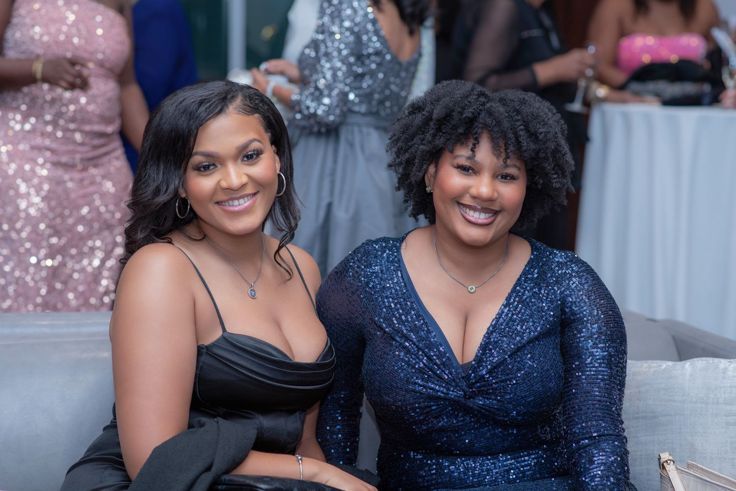 Two smiling women in elegant dresses posing together at a formal evening event.