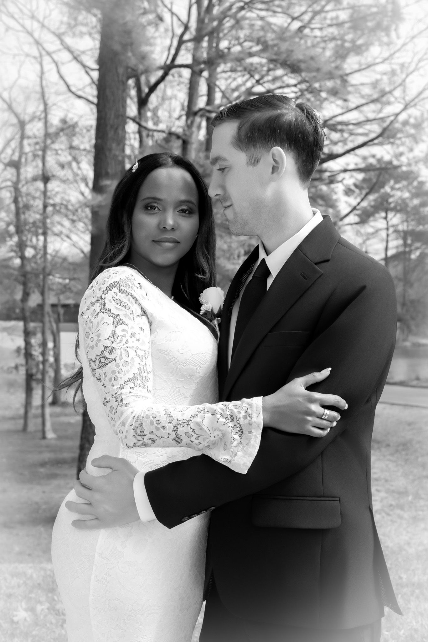 Black and white portrait of an interracial bride and groom embracing outdoors on their wedding day.