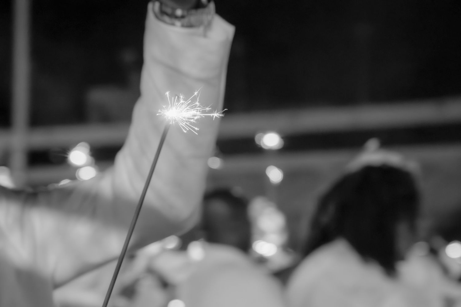 Black and white photo of a hand holding a lit sparkler at a celebration event.