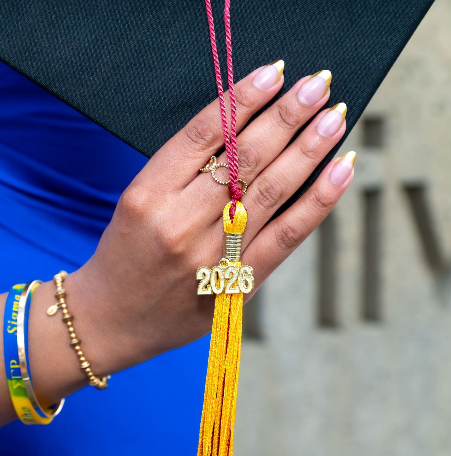 Close-up of a hand holding a 2023 gold graduation tassel with manicured nails and bracelets.
