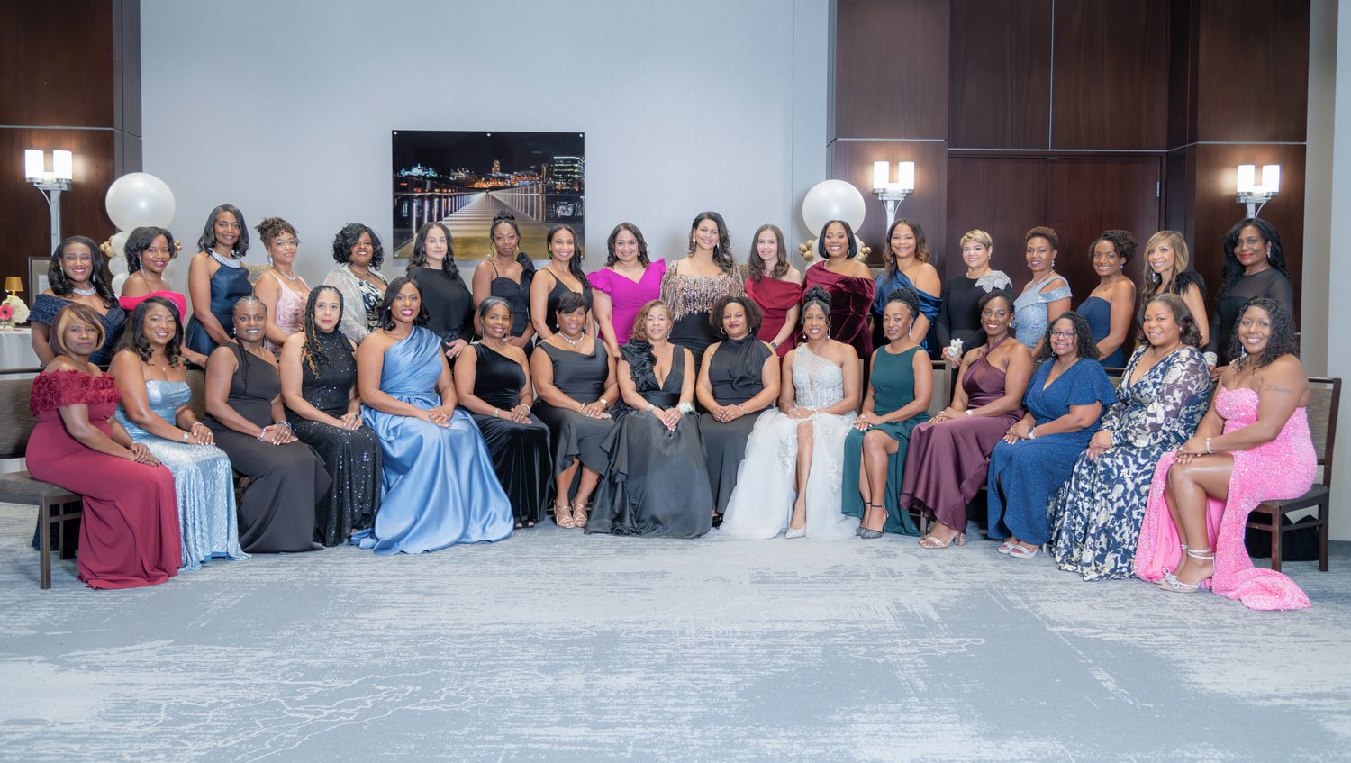 Large group of elegantly dressed women posing together at a formal event in a beautifully decorated venue.