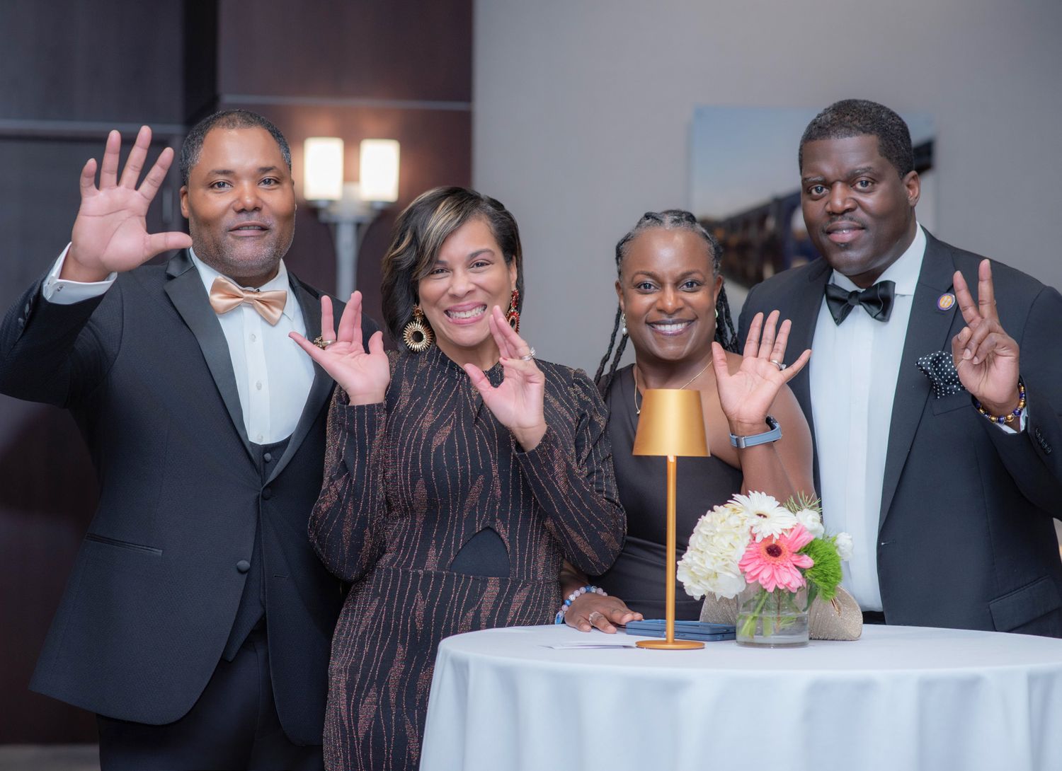 Four people smiling and posing with raised hands around a table at a formal gala event.