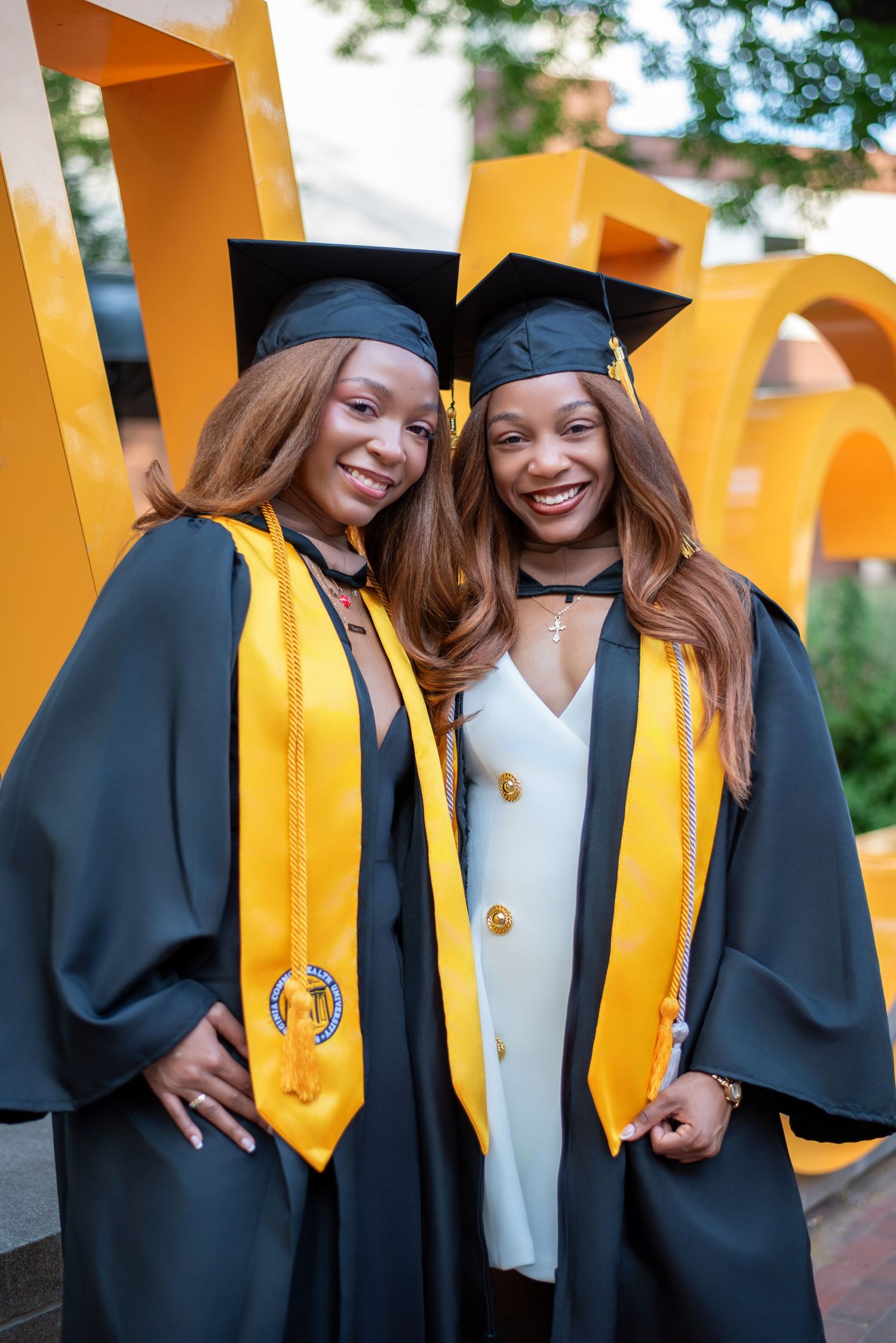 Two smiling graduates in black and gold caps and gowns posing together at their graduation ceremony.