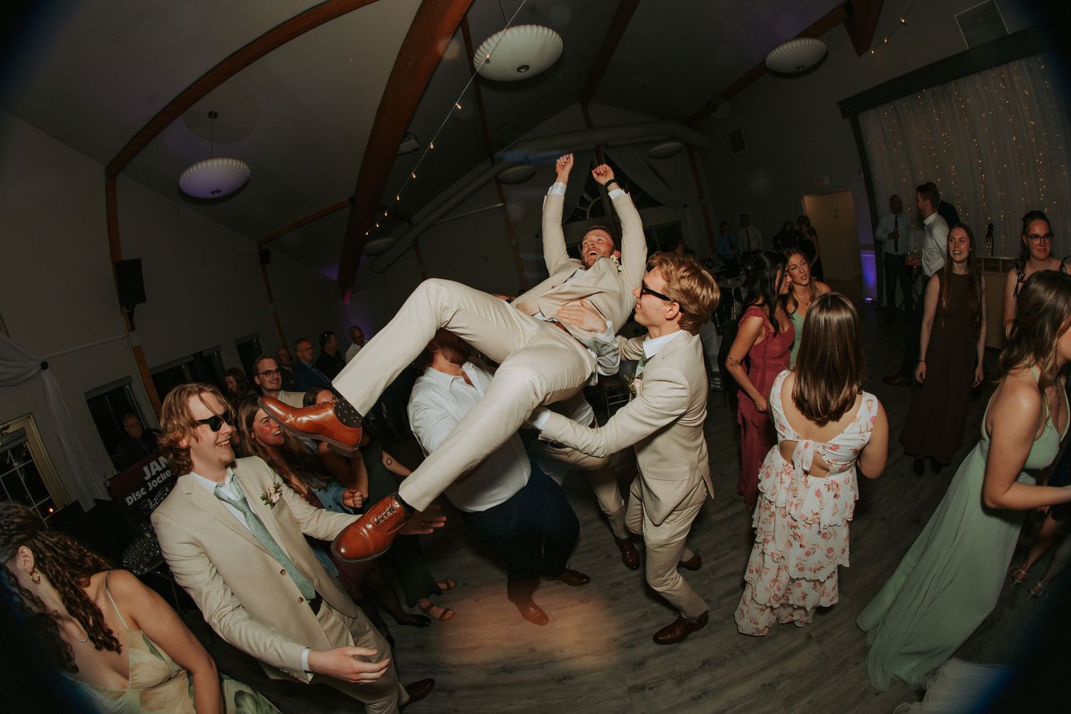 Guests dancing energetically at a wedding reception, with one person being lifted in the air on a festive dance floor.