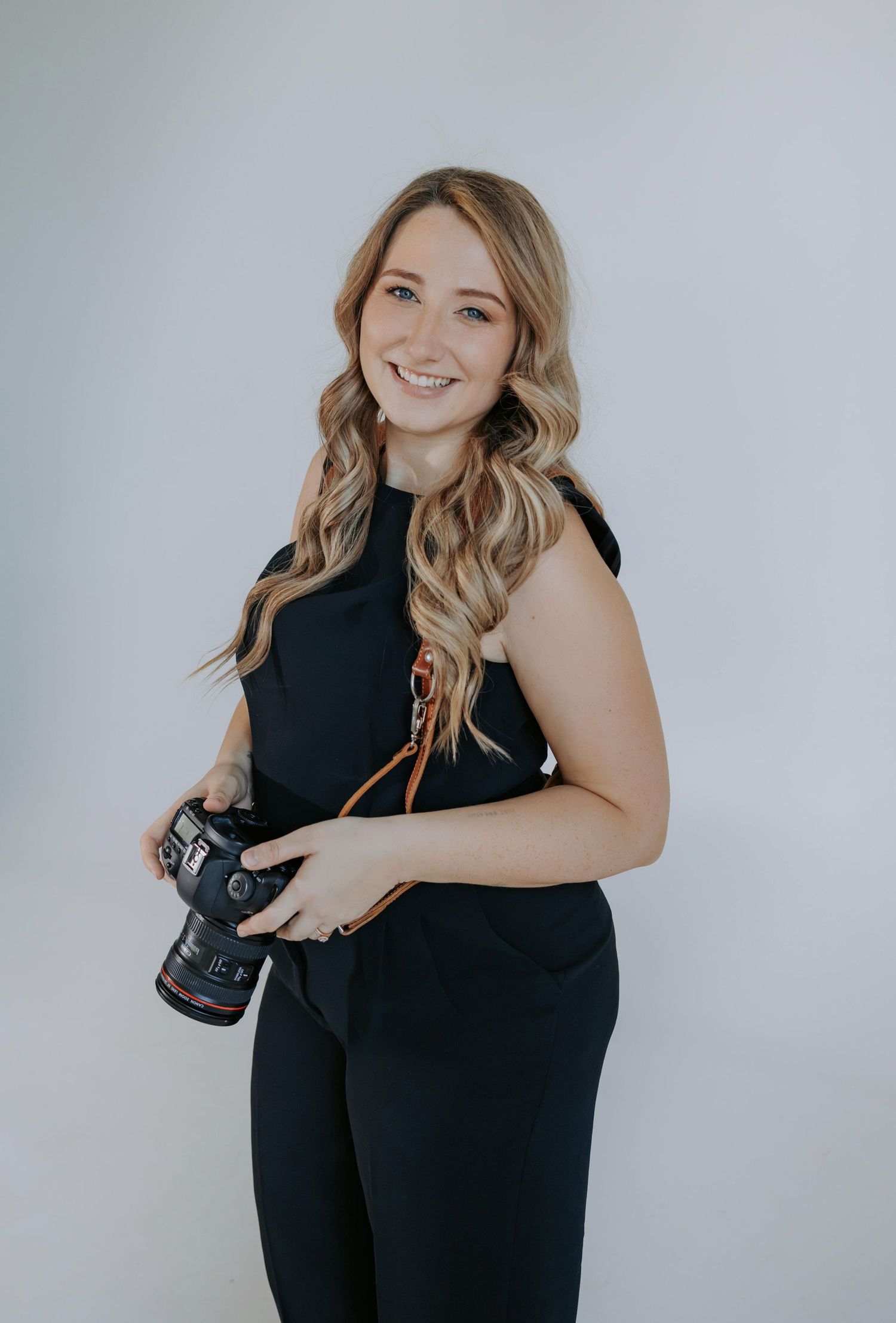 Professional photographer in black dress poses with camera against white studio backdrop showing various angles and expressions.
