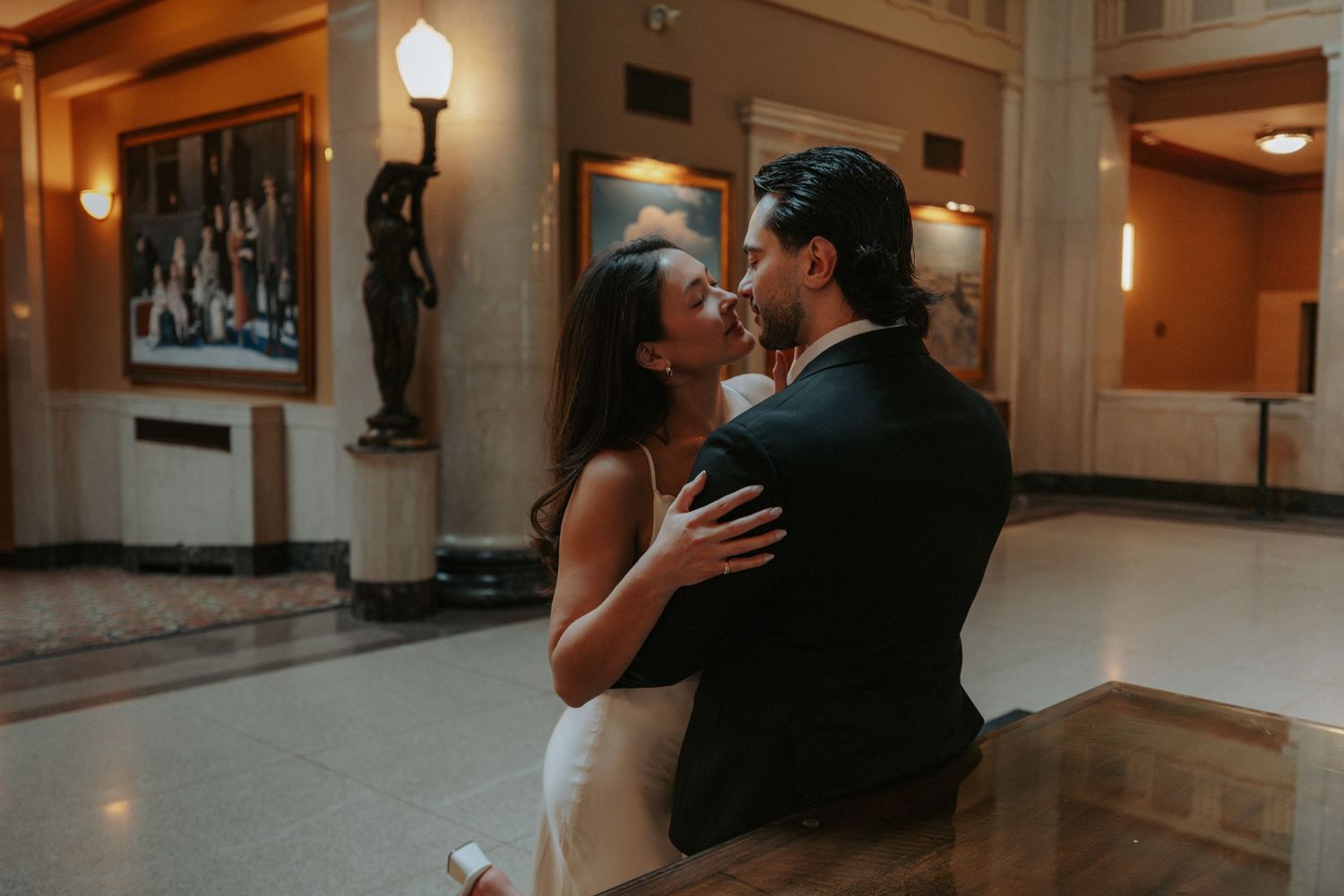 Couple sharing a romantic moment in an elegant hotel lobby, dressed in wedding attire.