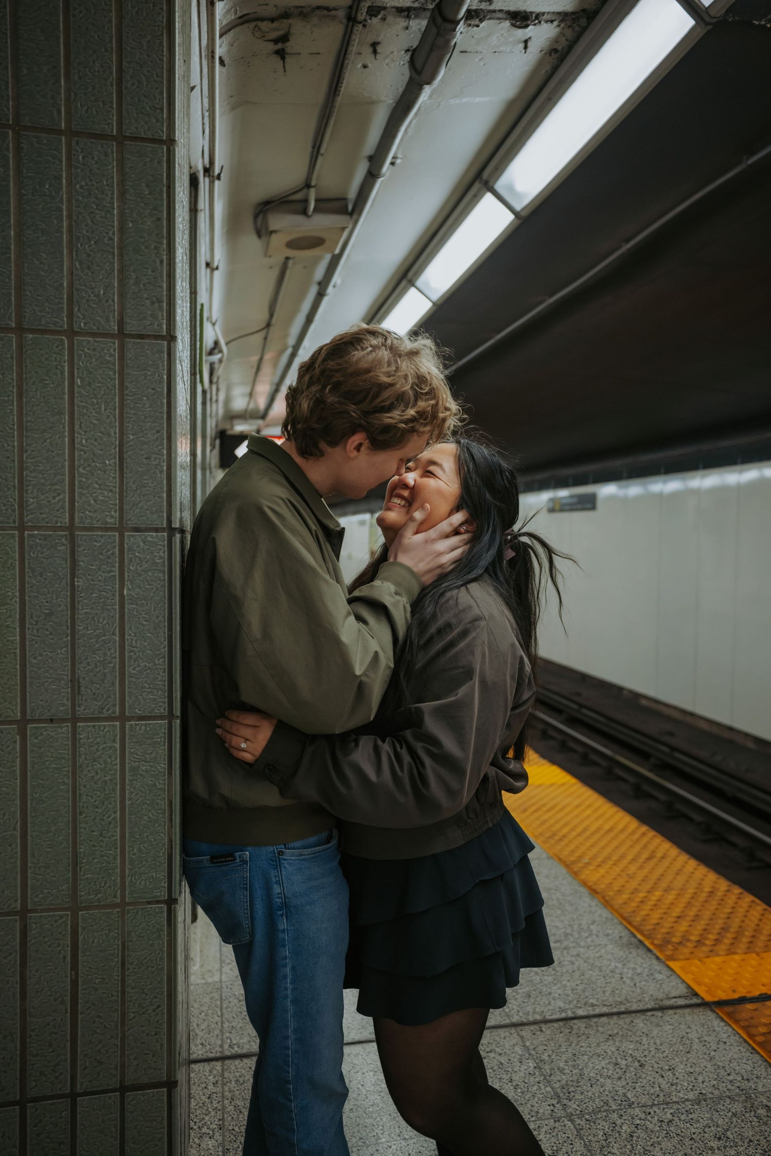 Couple sharing a romantic moment on a subway platform, embracing and smiling at each other near the yellow safety line.