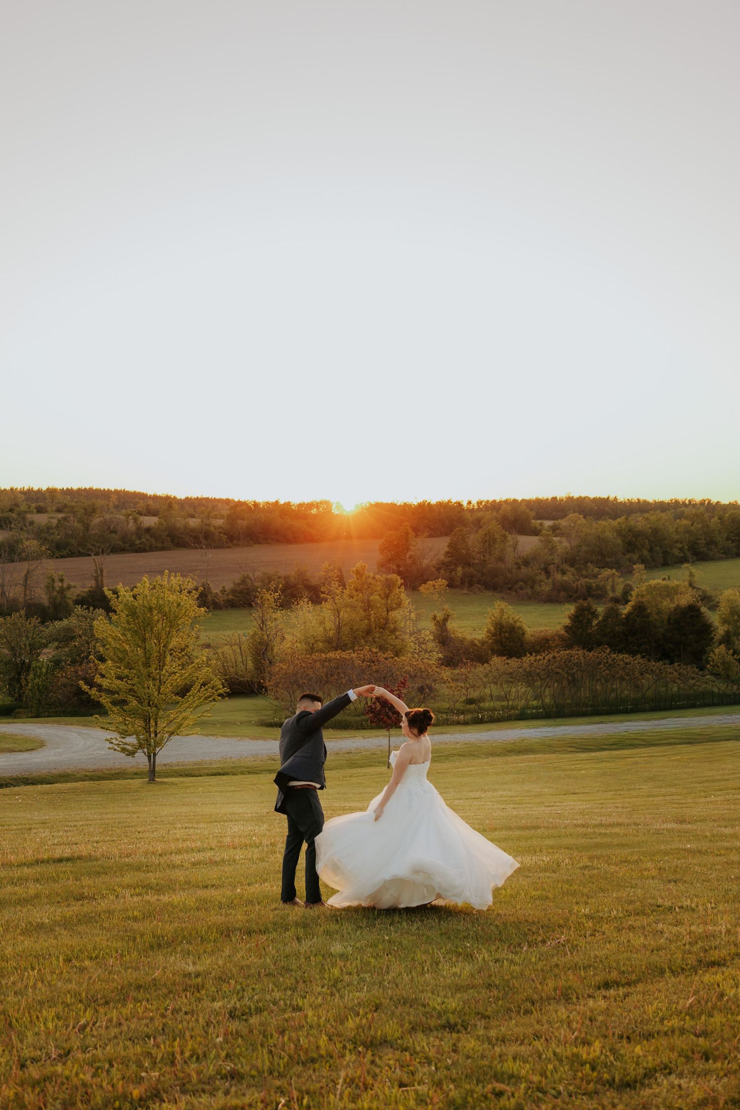 Bride and groom dancing at sunset on a lush green field with rolling hills in the background.