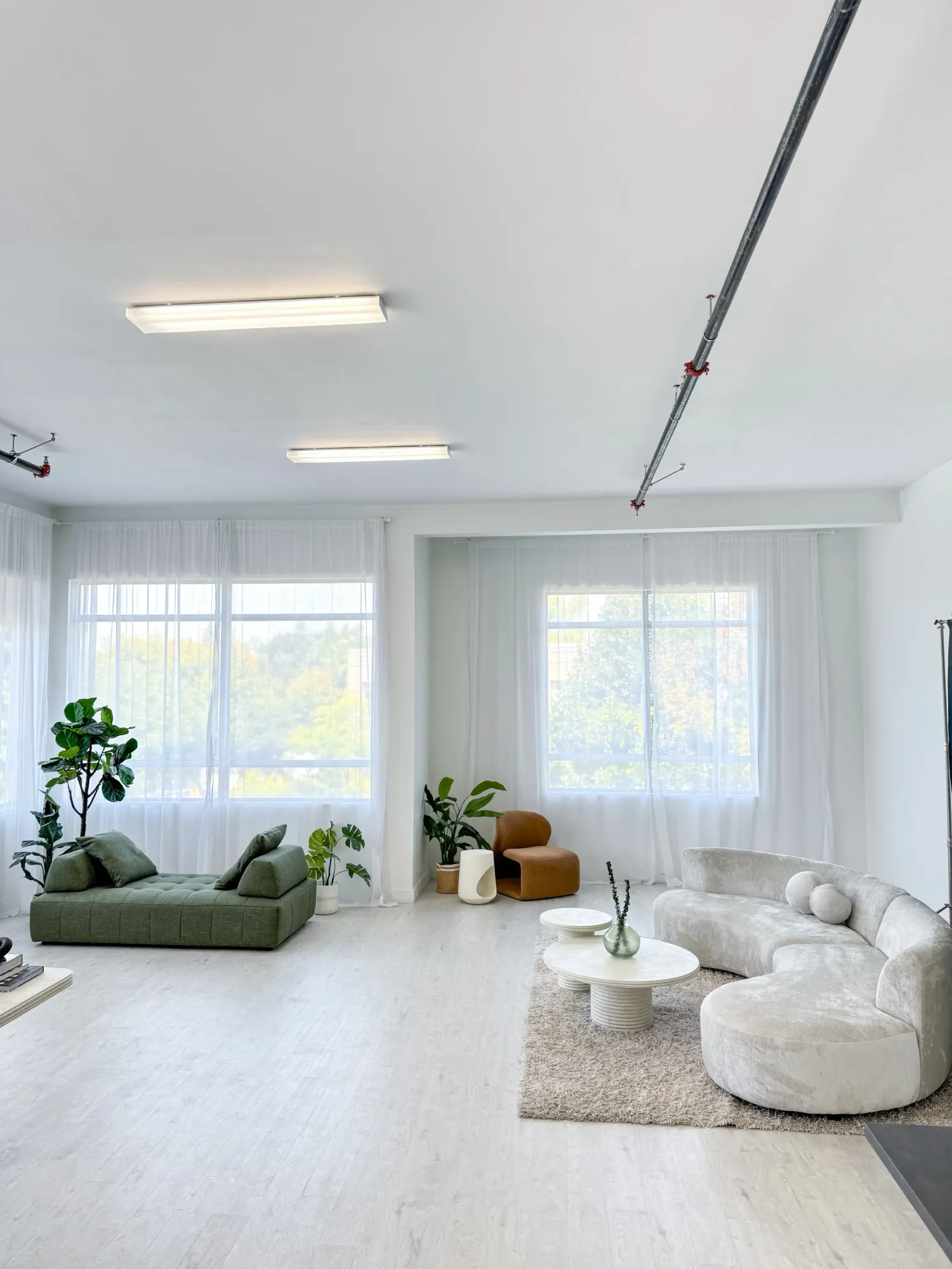 Bright minimalist studio space with white walls, green daybed, and sheer curtains filtering natural light. MDRN Studio, Ottawa