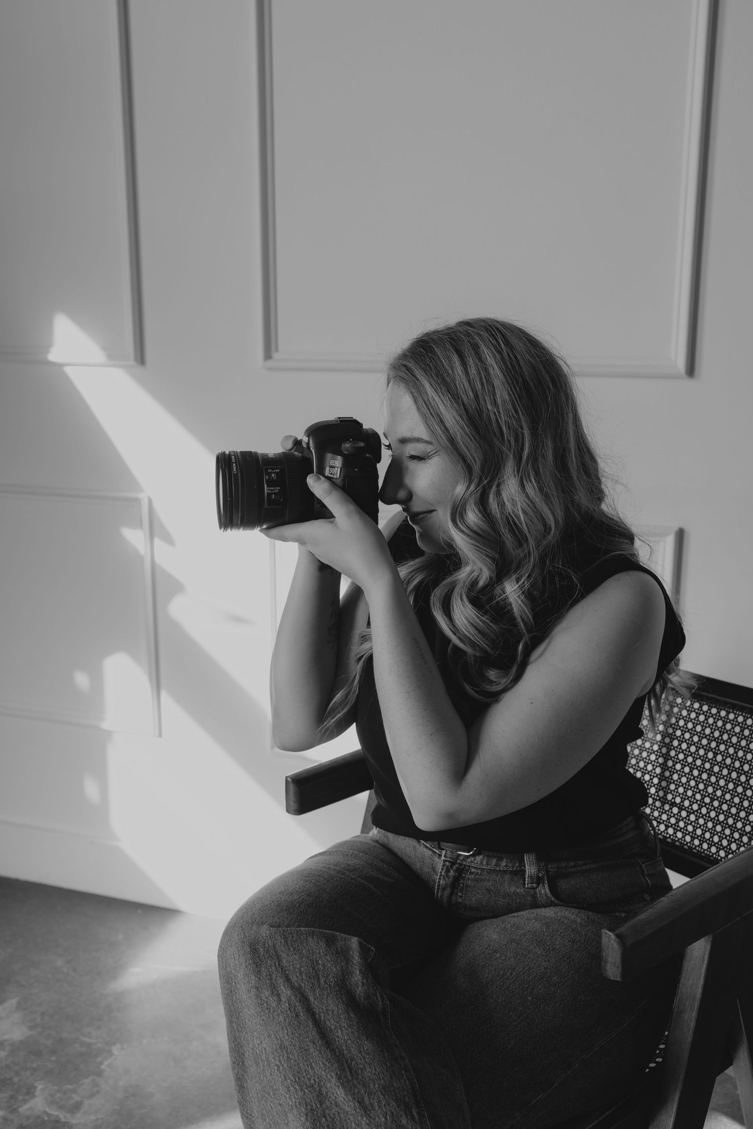 A photographer sits in profile view taking pictures with a camera in a minimalist black and white setting.