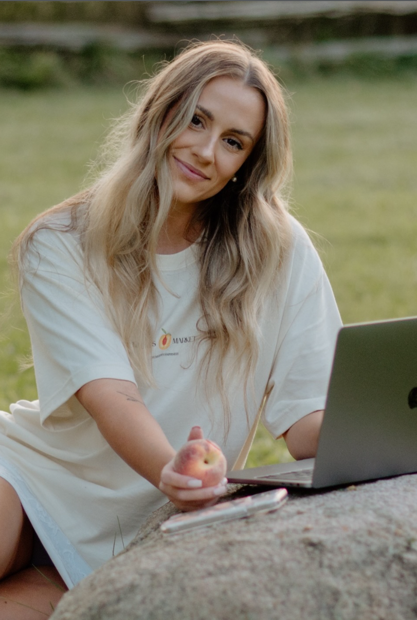 Student in white t-shirt working on laptop outdoors while taking notes and studying in natural lighting.