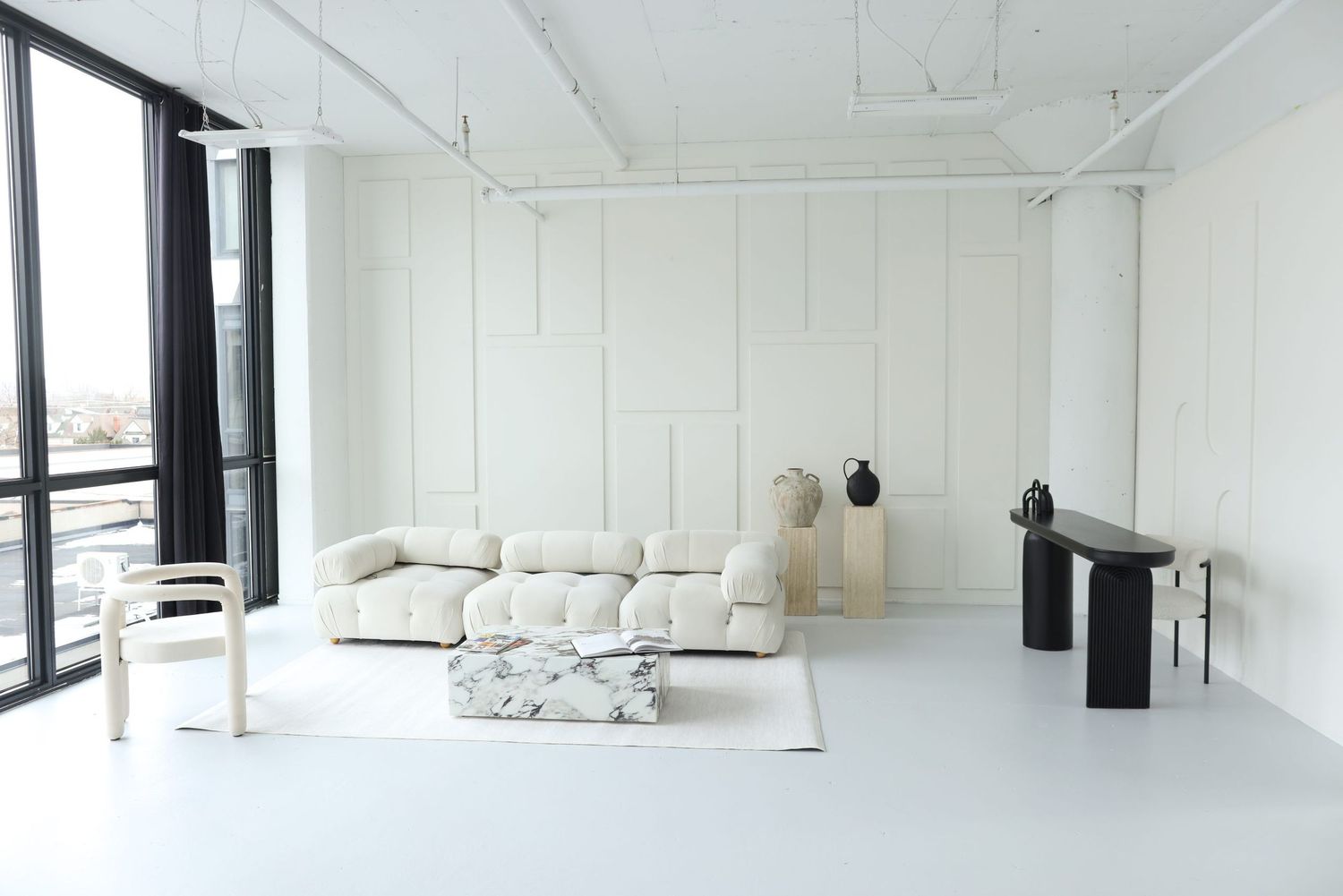 A bright, minimalist white interior space with large windows and black structural beams along the ceiling. Icon Studio, Toronto
