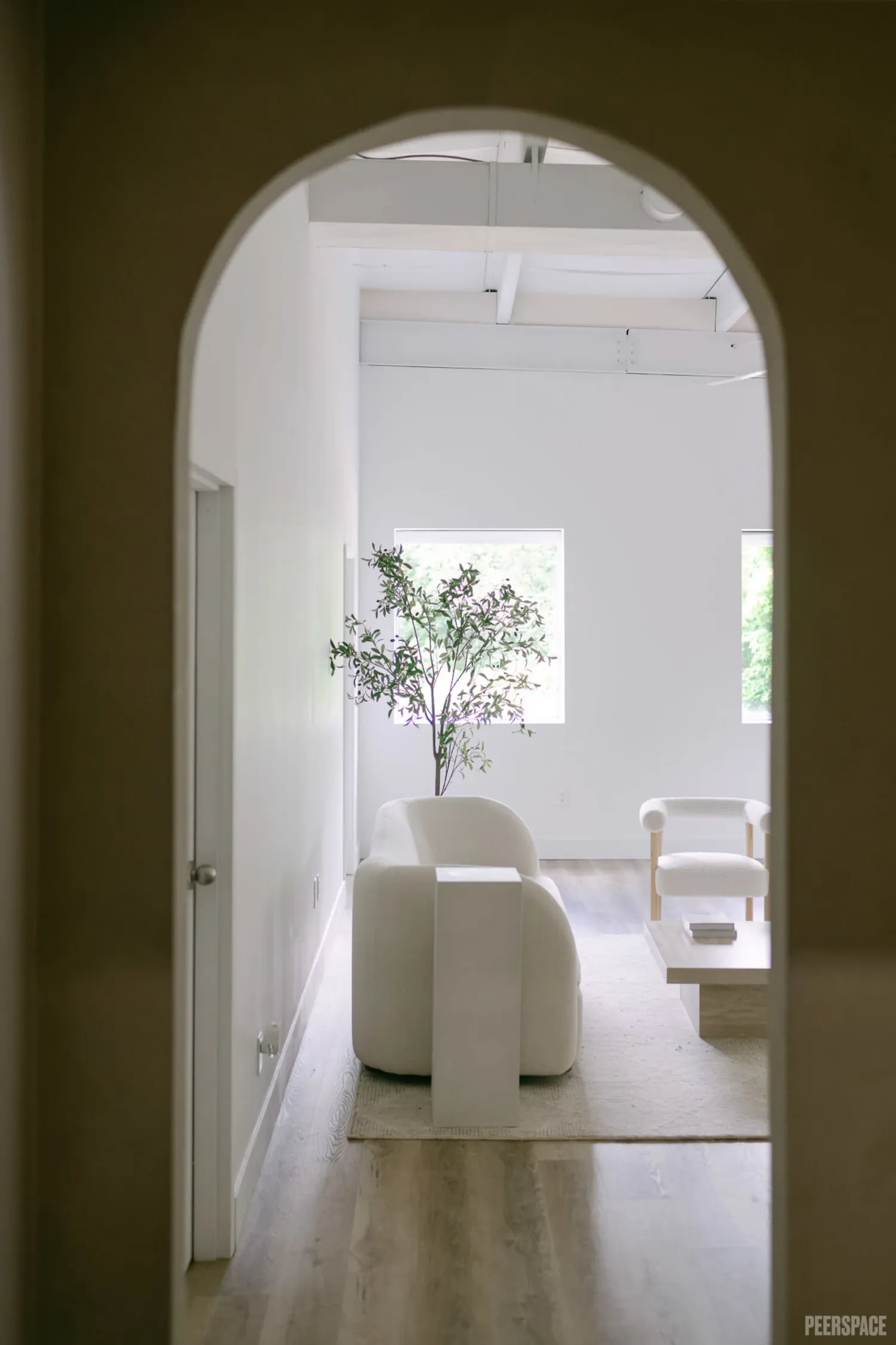 A minimalist white interior hallway with arched doorways and wooden floors leading to a bright sunlit room. Studio Saint Eden Burlington