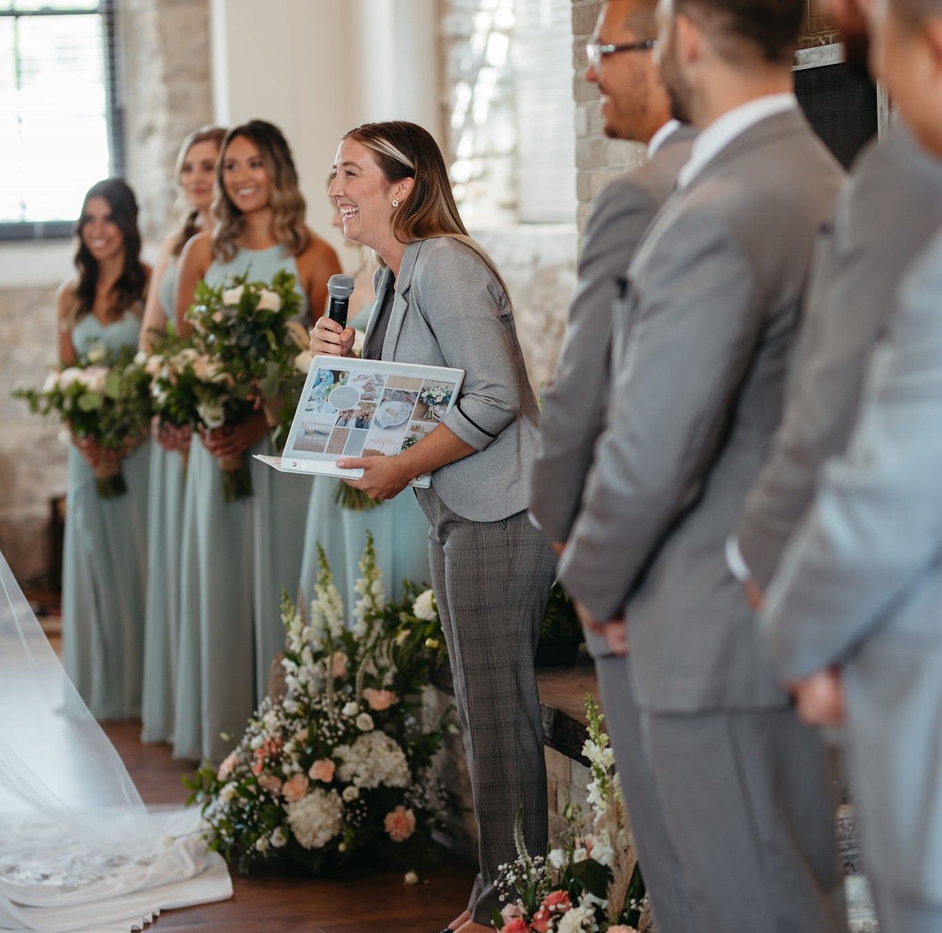 Wedding party in gray suits and sage green dresses gather during ceremony with elegant floral arrangements.