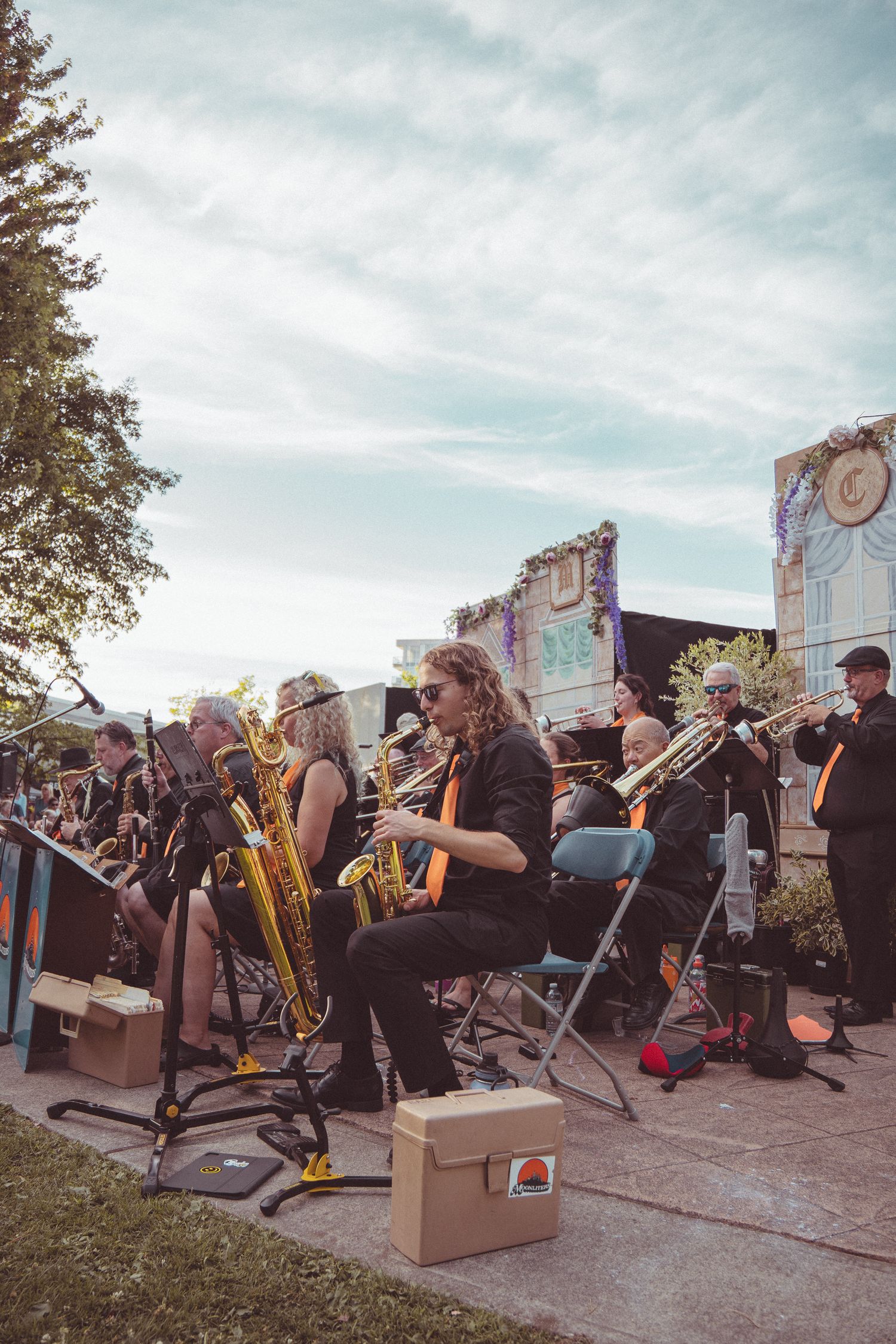 Outdoor jazz band performs live with saxophones and trumpets under a cloudy sky at a festive event.