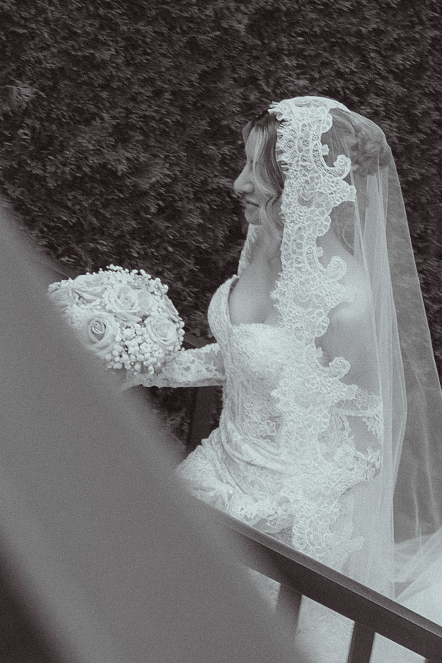 Black and white photo of a bride in lace wedding dress and veil holding a white rose bouquet.