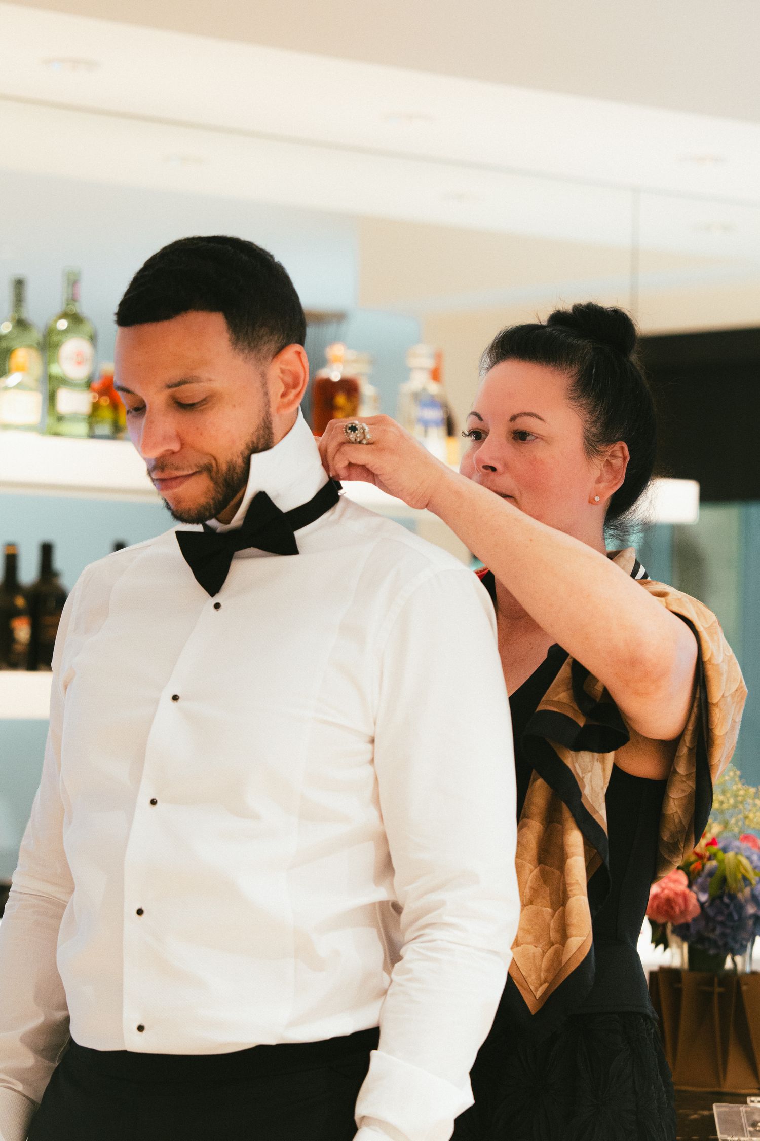 Woman adjusting bow tie on man in white tuxedo shirt at formal event.