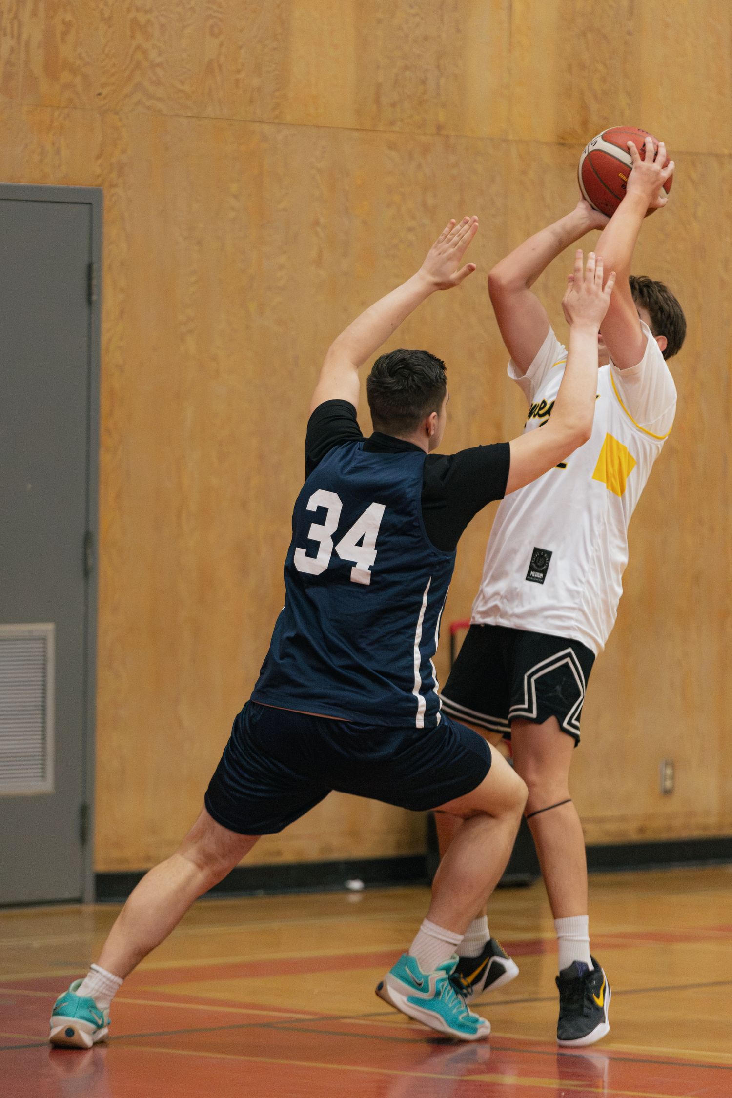 Player 34 in dark jersey contests a ball possession against opponent in white during indoor game.