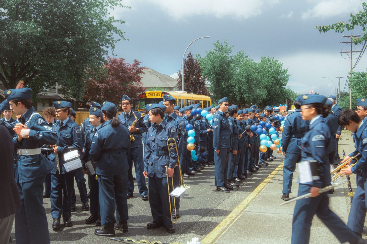 Air cadets in blue uniforms assemble on a suburban street with a school bus visible in background.