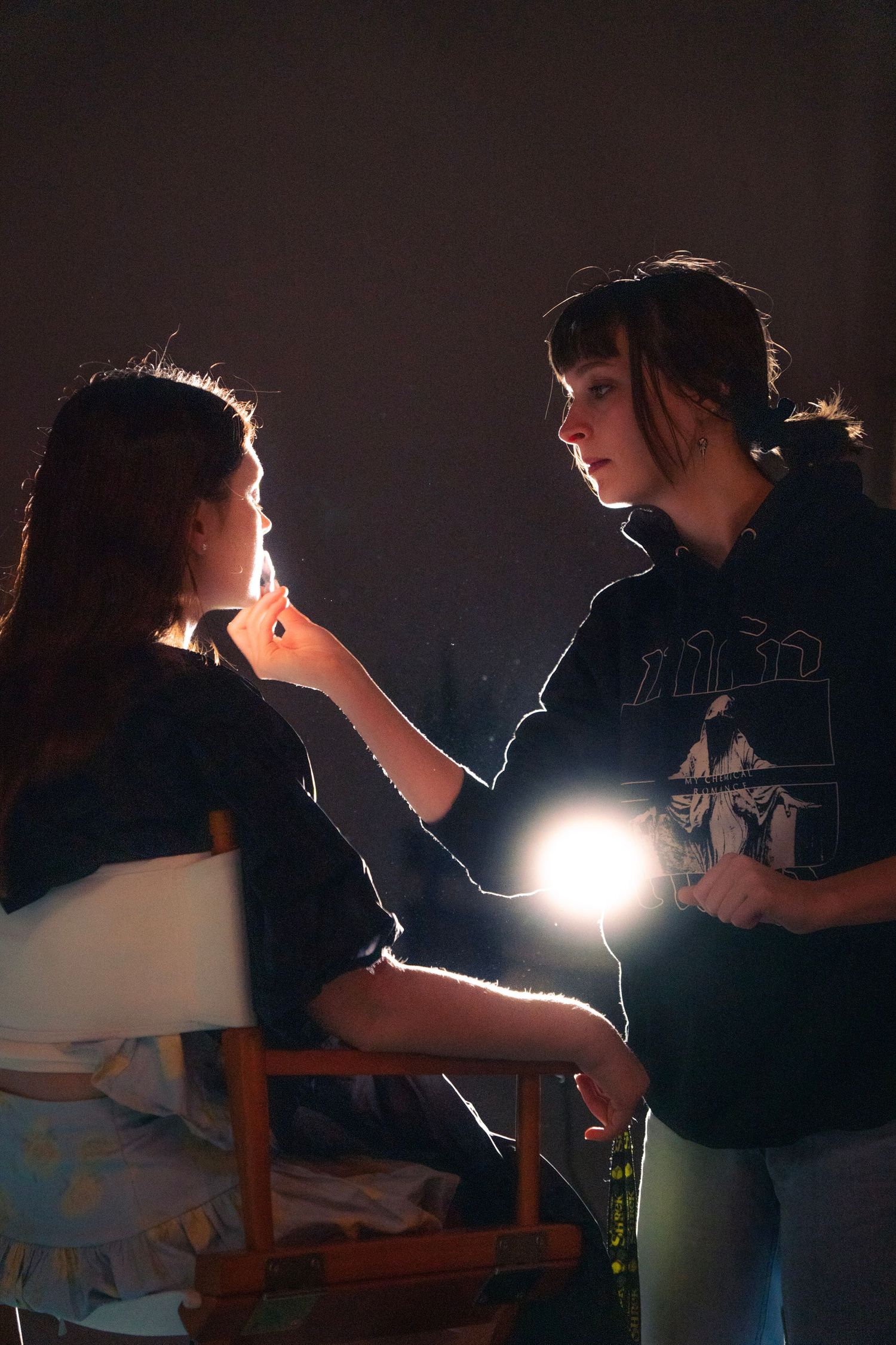 Makeup artist applying lip color to actress using a handheld light in a dark studio.