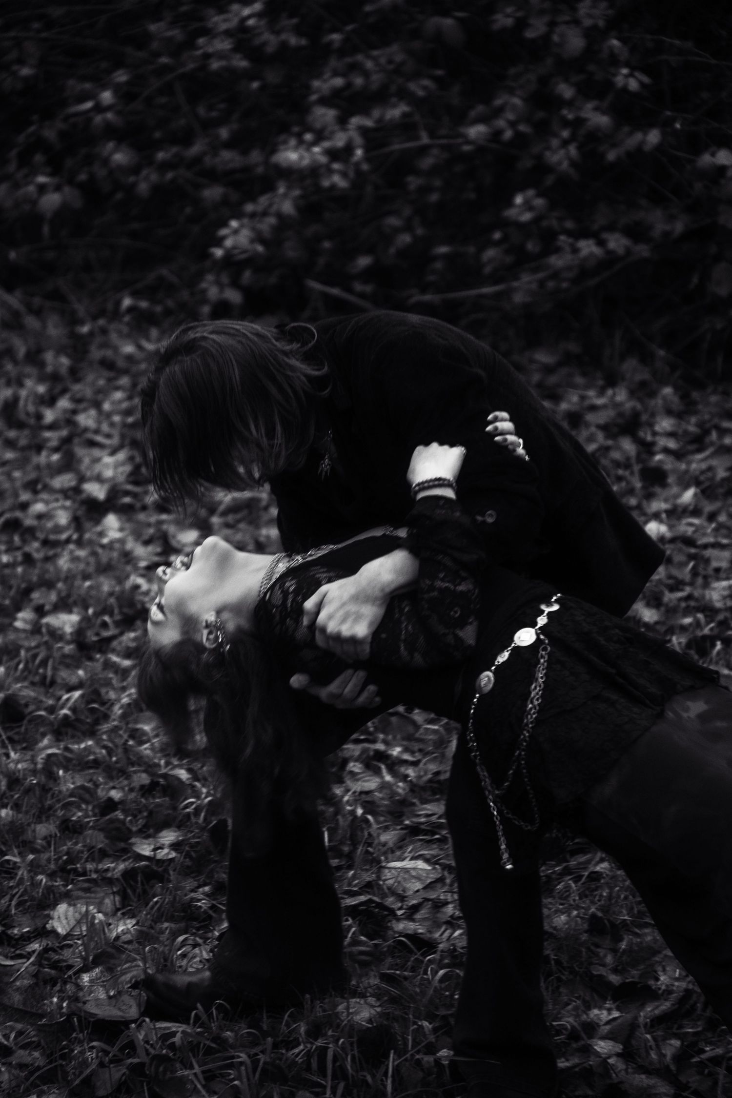 Black and white photo of gothic couple in dramatic pose among fallen leaves.