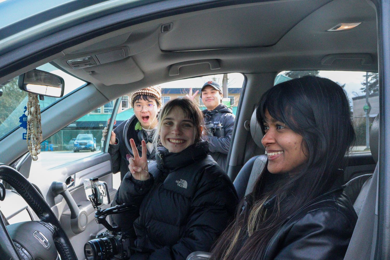 Four smiling people inside a vehicle during a film production shoot.