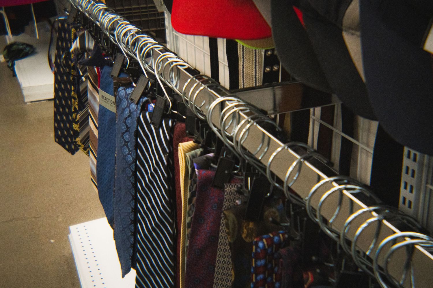 Row of assorted neckties hanging on a metal rack in a thrift store clothing department.