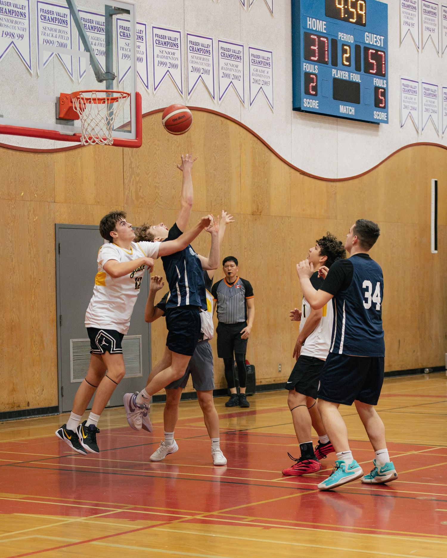 Indoor basketball game with players driving to the hoop as scoreboard shows 37-57 with 4:59 remaining.