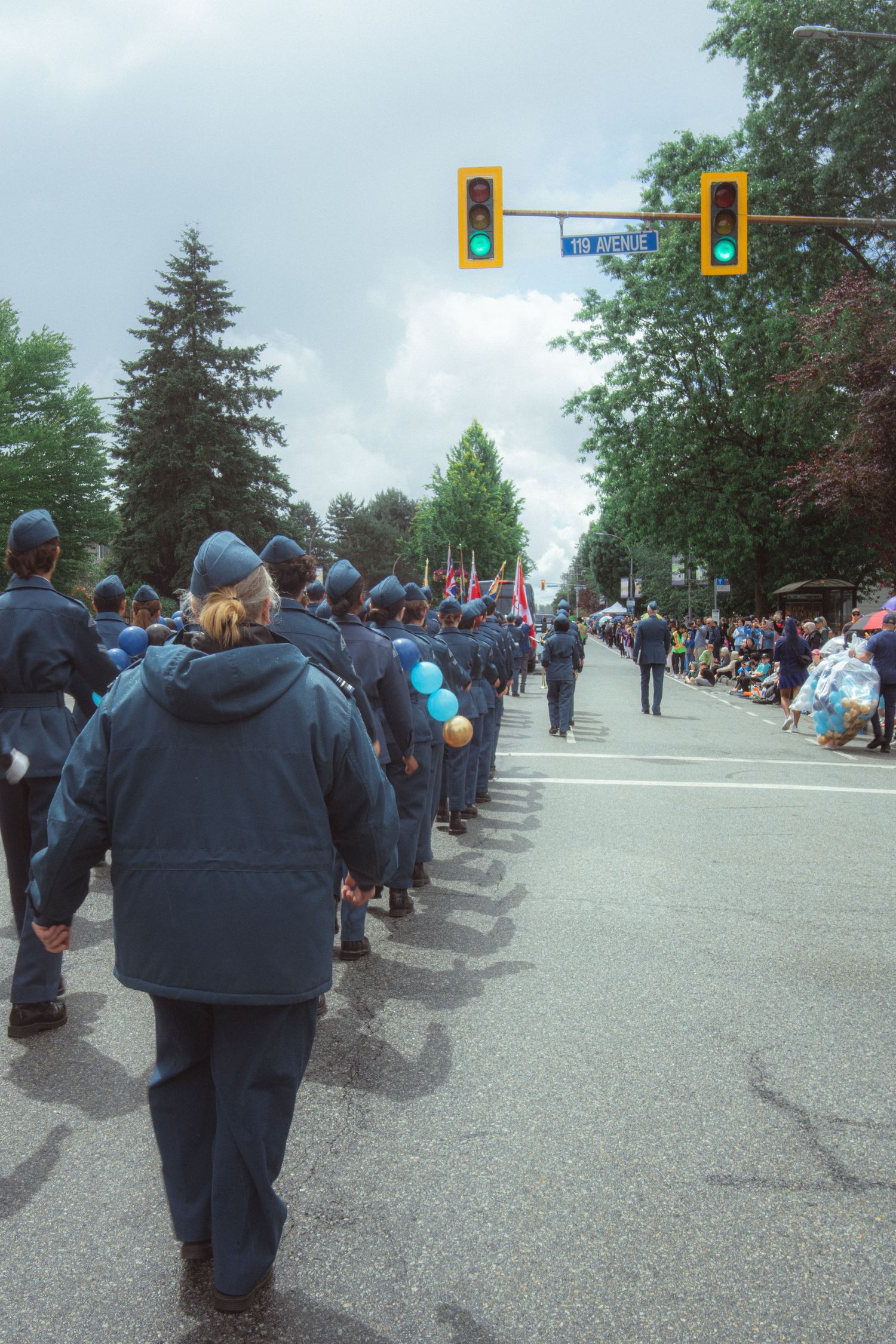 Air cadets in blue uniforms march down a parade route lined with spectators under grey skies.