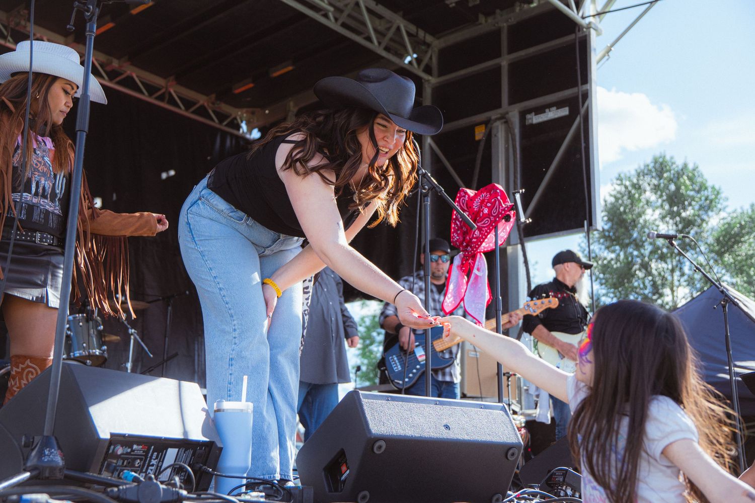 Country singer in black cowboy hat leaning off stage to connect with fan at outdoor music festival.