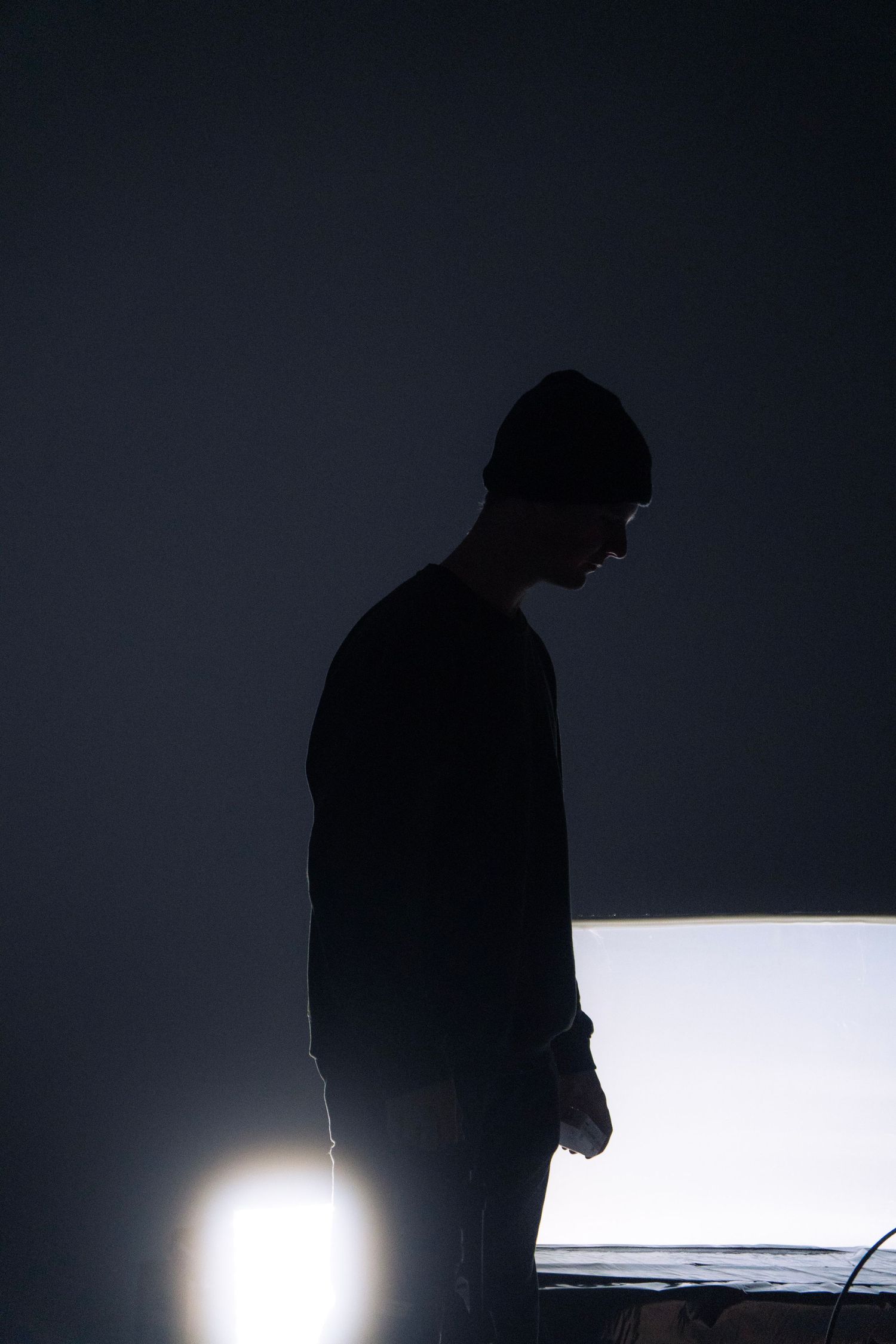 Silhouette of a man wearing a beanie standing in a dark studio with dramatic backlighting.