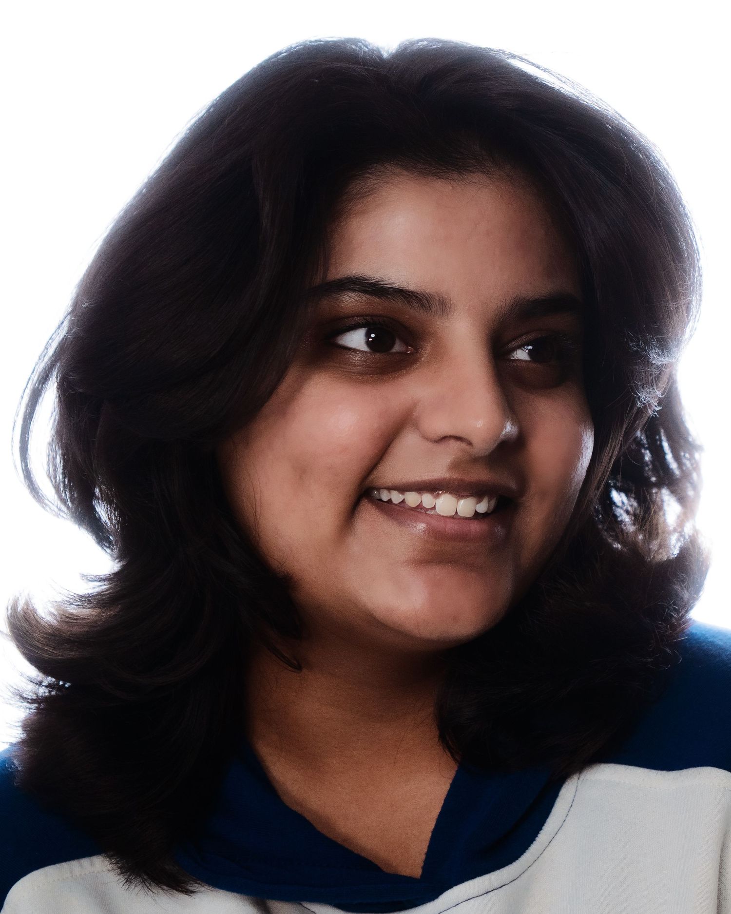 Smiling young woman with dark shoulder-length hair wearing a blue and white top against white background.