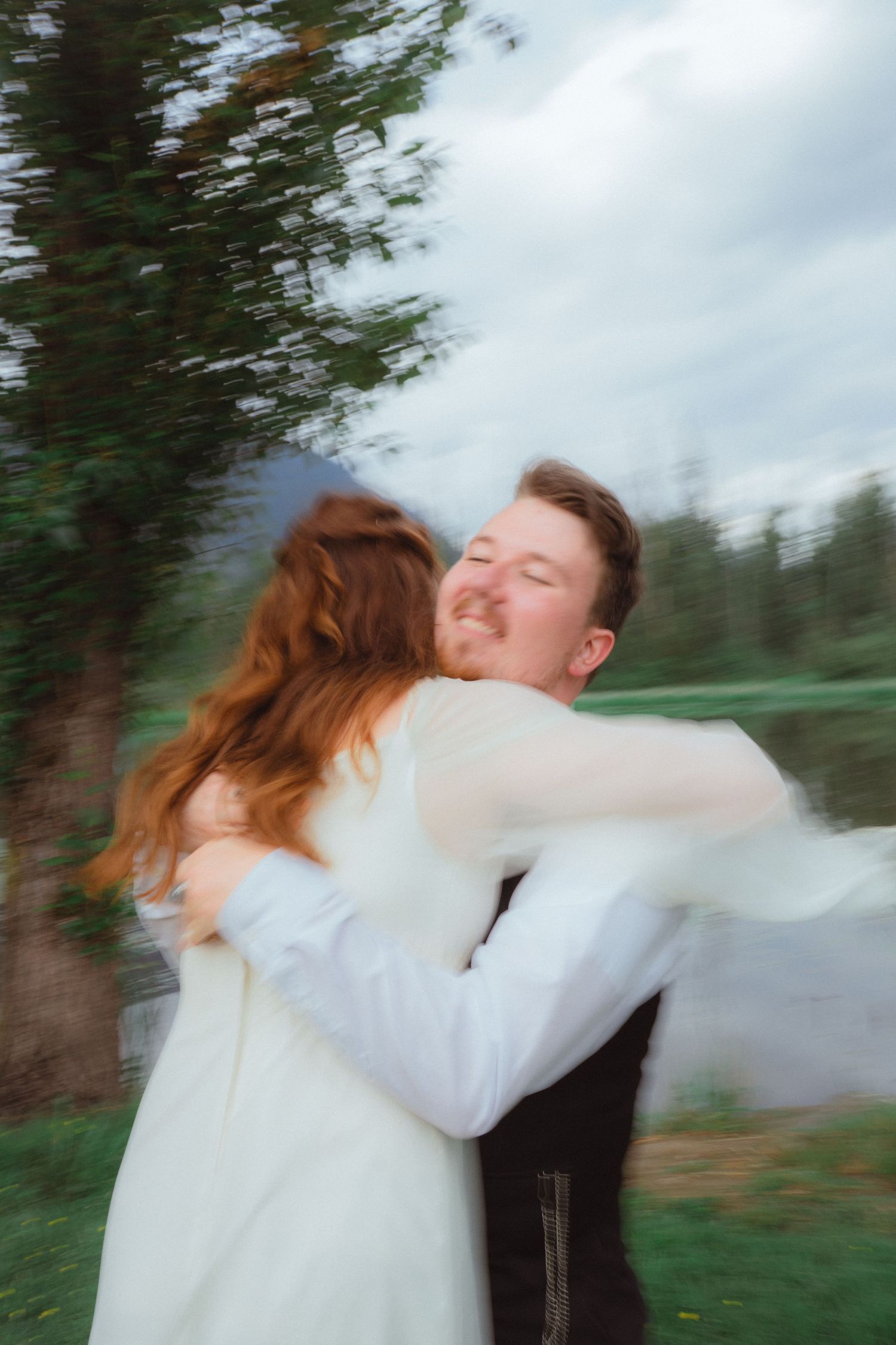 A couple shares a joyful spinning embrace outdoors near trees with motion blur effect.