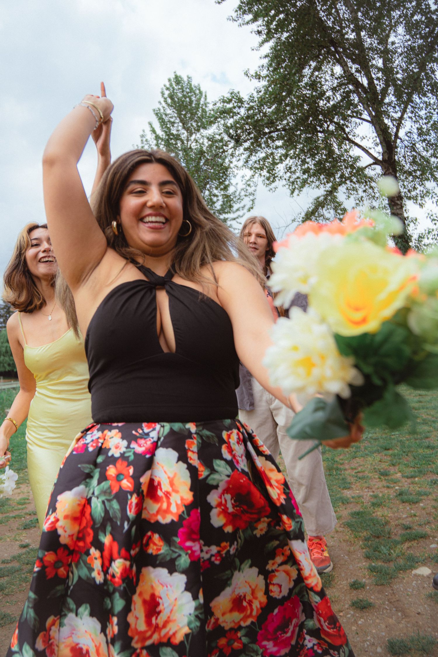 Joyful wedding guest in floral skirt catches bouquet toss at outdoor celebration.