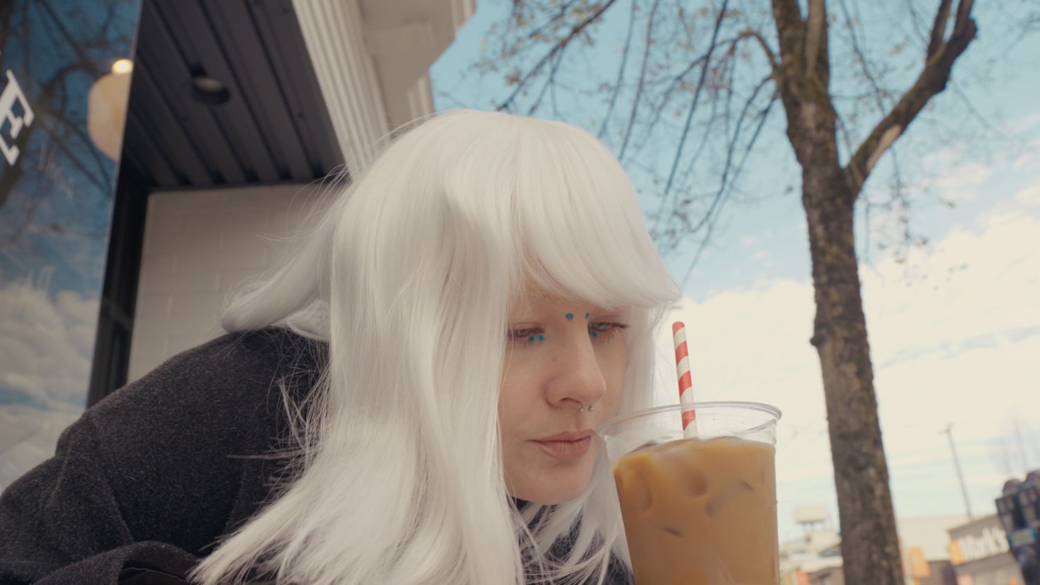 Woman with white hair sipping iced coffee outdoors at a cafe.