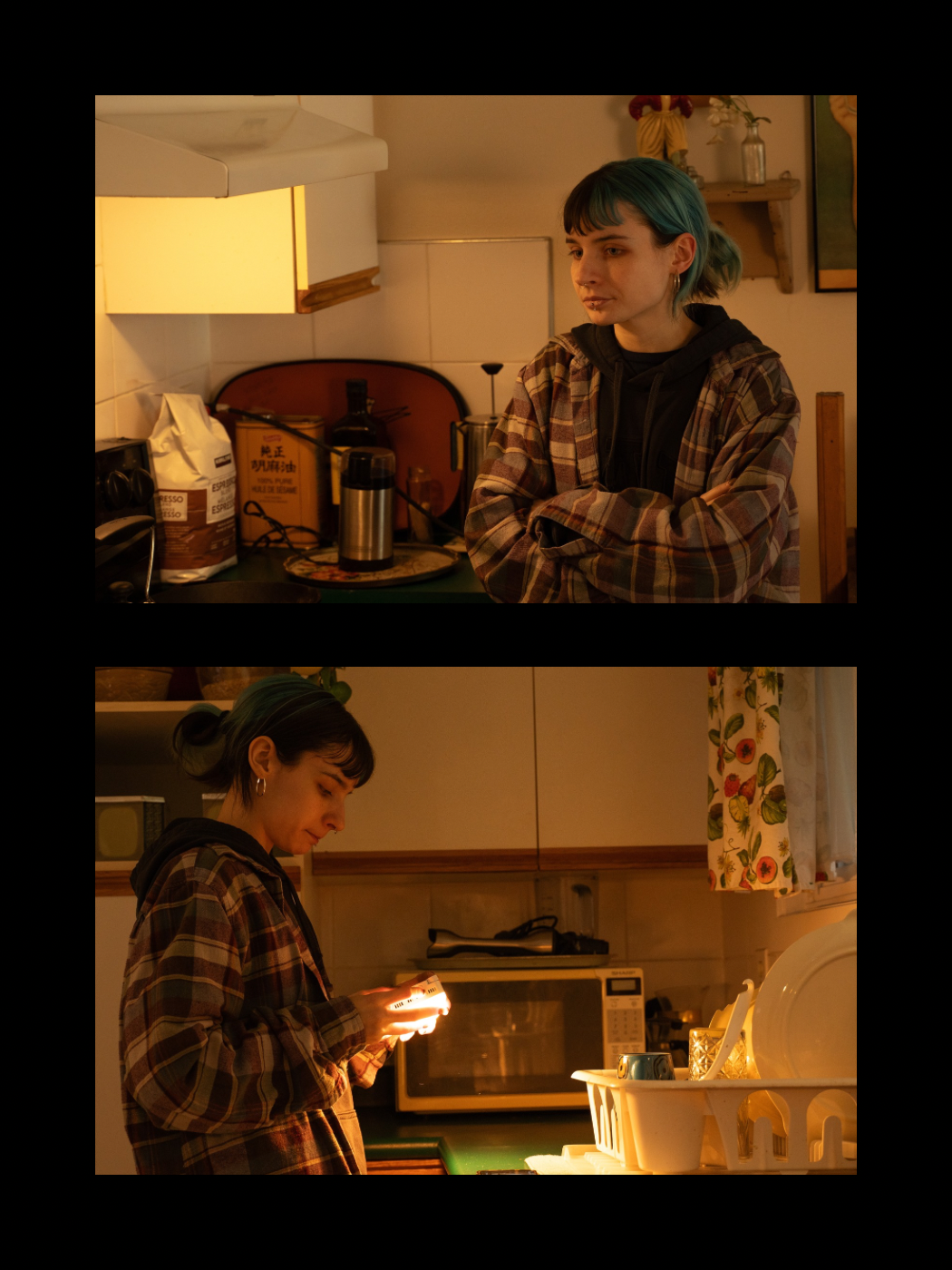 A young woman with teal hair sits pensively in a warmly lit kitchen while another person checks their phone.