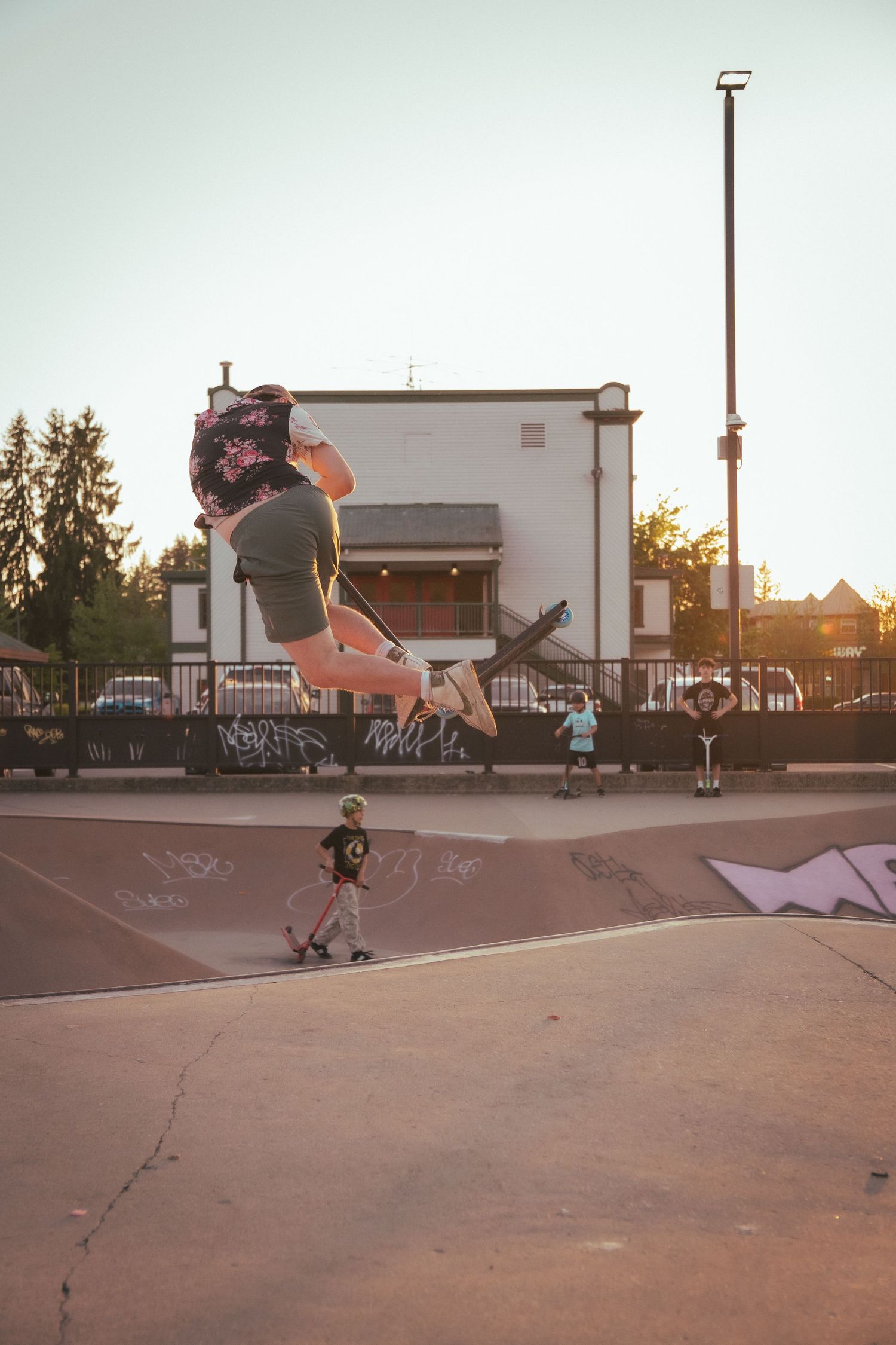Skateboarder performing a high jump trick at an outdoor skate park during golden hour sunset.