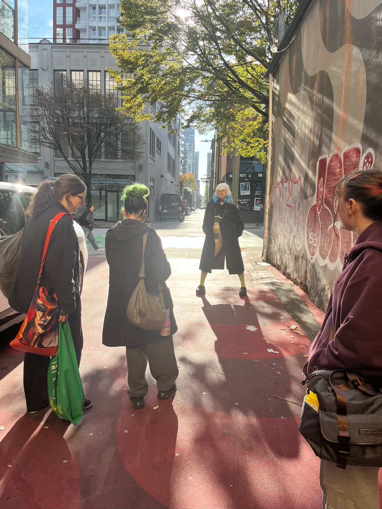 Group of people gathered on a red sidewalk next to a graffiti wall in a city.