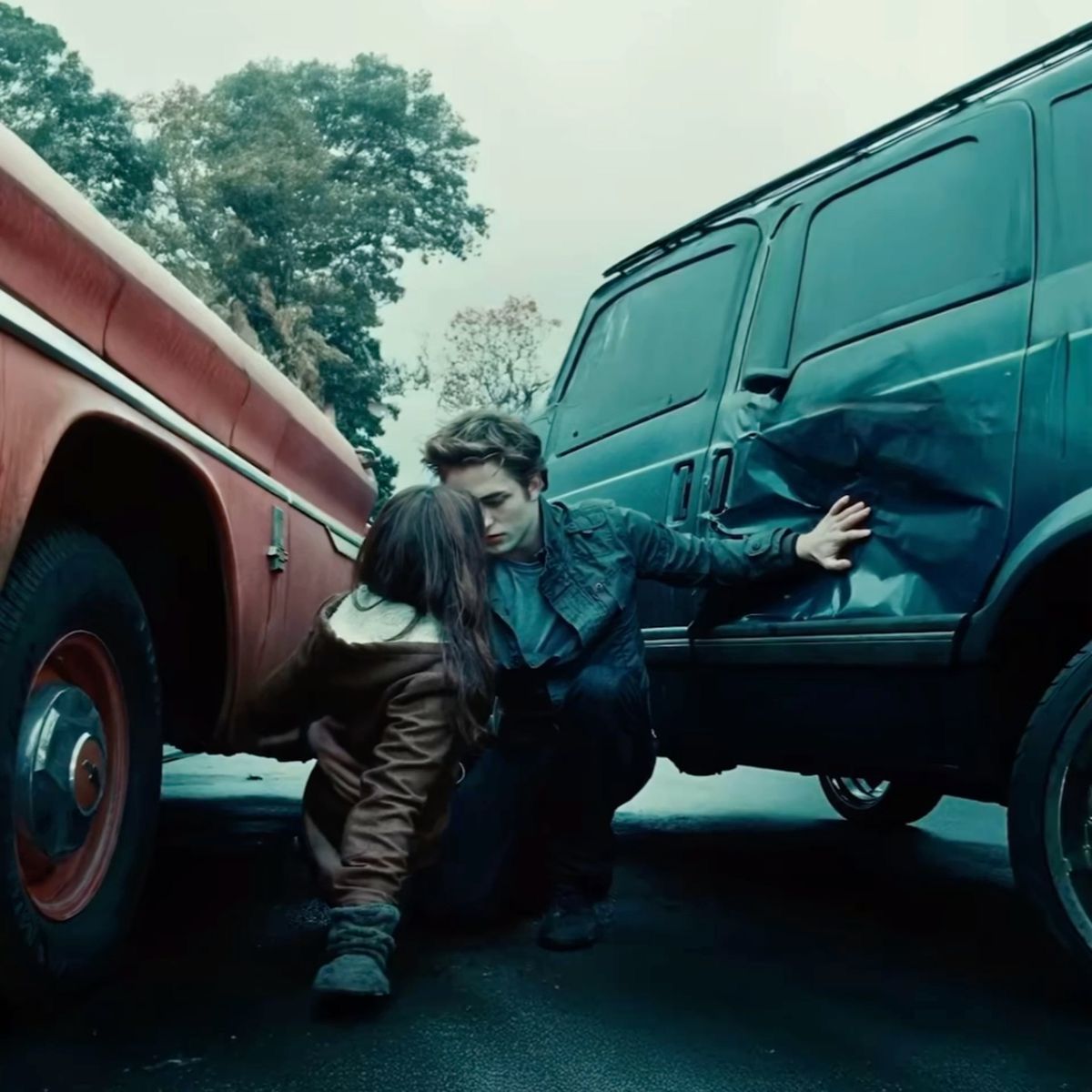 A person in a black jacket shields another between two vehicles in a dramatic outdoor scene.