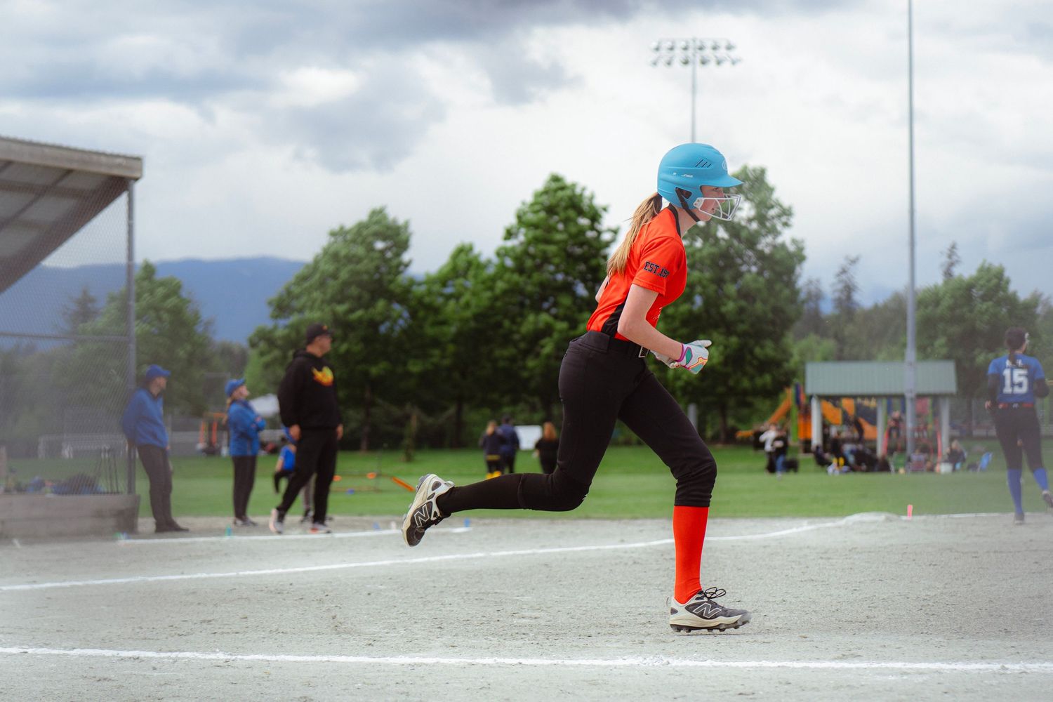 Young female softball player sprinting along the baseline in an orange uniform.