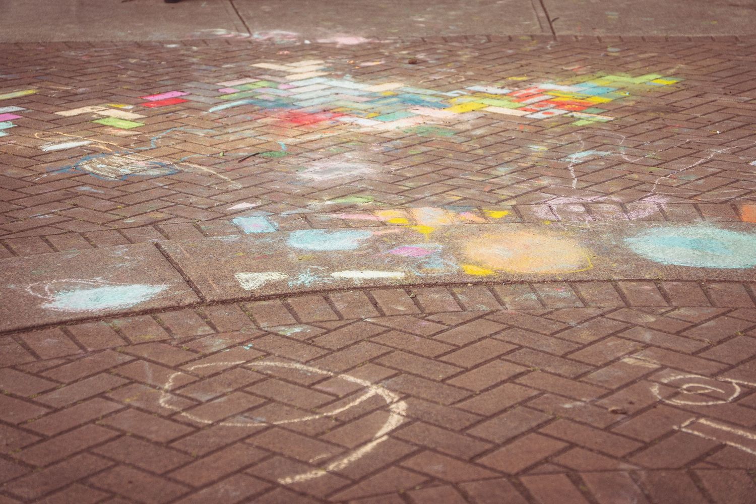 Colorful chalk art drawings on a red brick pavement outdoor plaza floor.