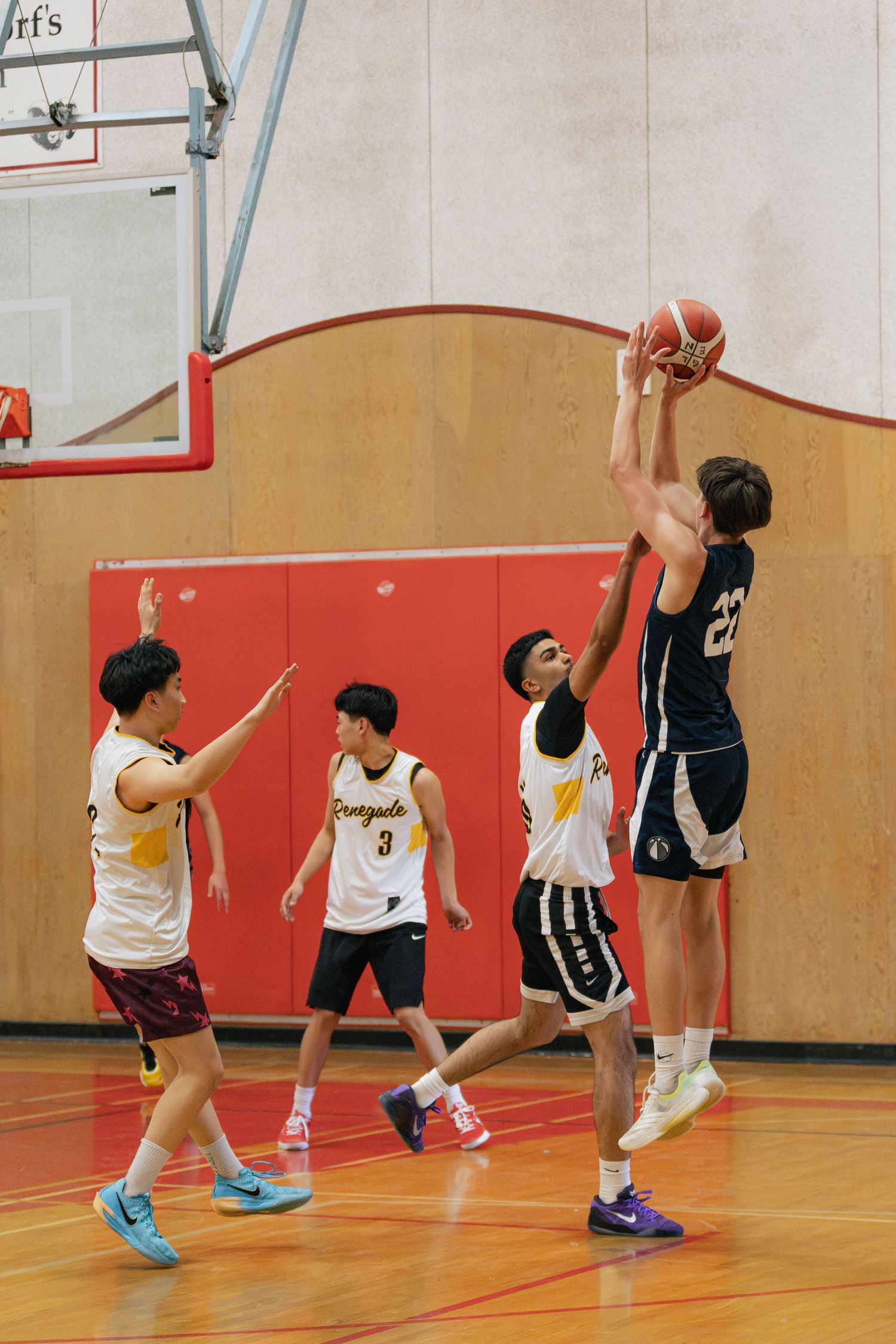 Player #22 in navy uniform jumps to catch basketball while defenders in white Renegades jerseys attempt to block during indoor game.