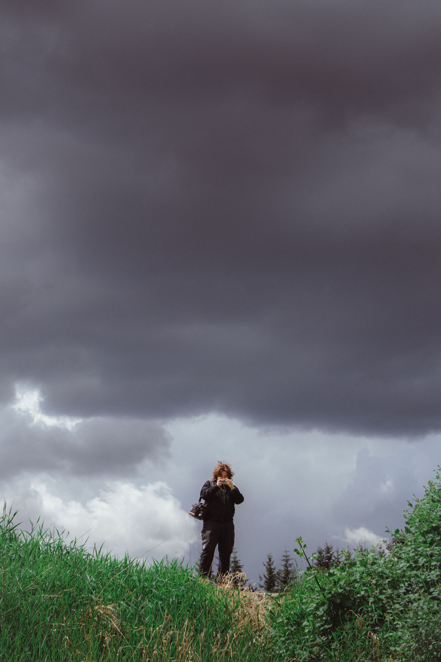 Person standing on a grassy hilltop under dramatic dark storm clouds in a moody landscape.