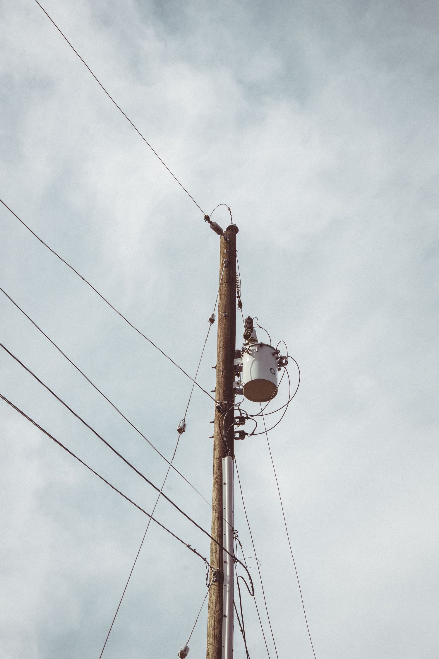 Wooden utility pole with transformer and power lines against an overcast cloudy sky from low angle view.